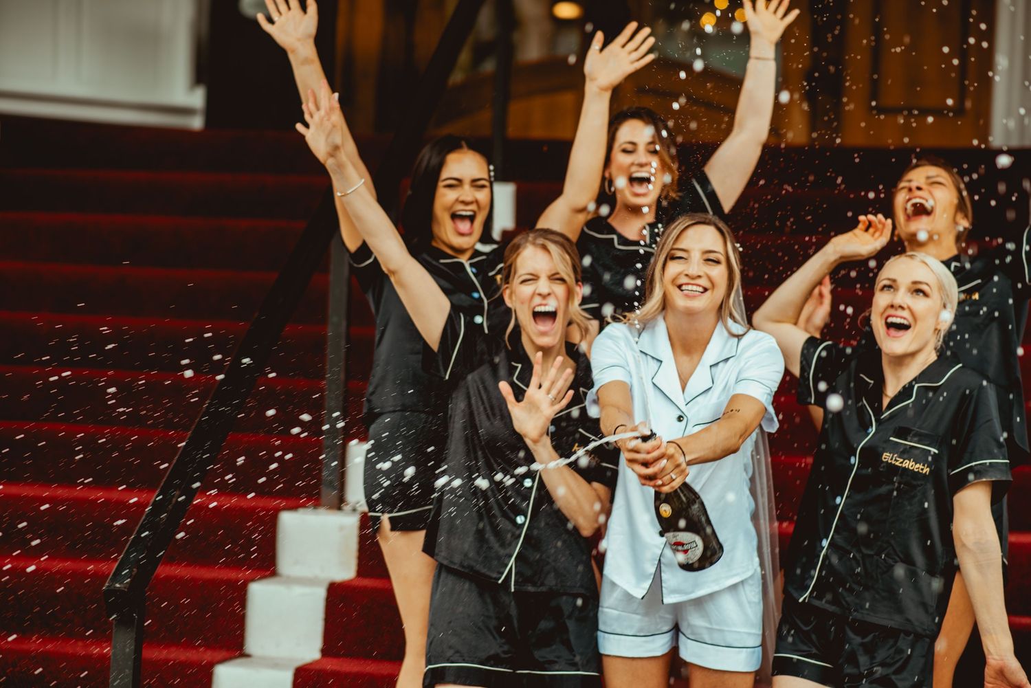 Wedding party celebrates with arms raised in excitement at an indoor venue.