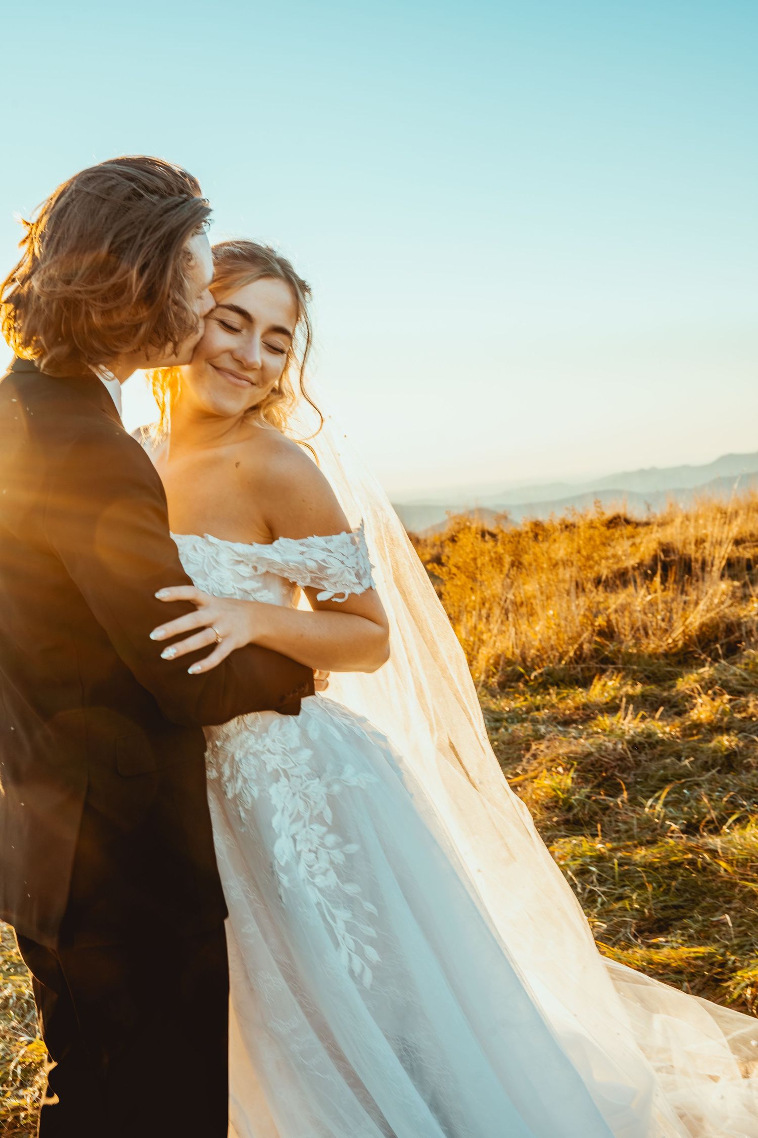 A romantic wedding photoshoot at sunset with a flowing white dress against golden mountain scenery.