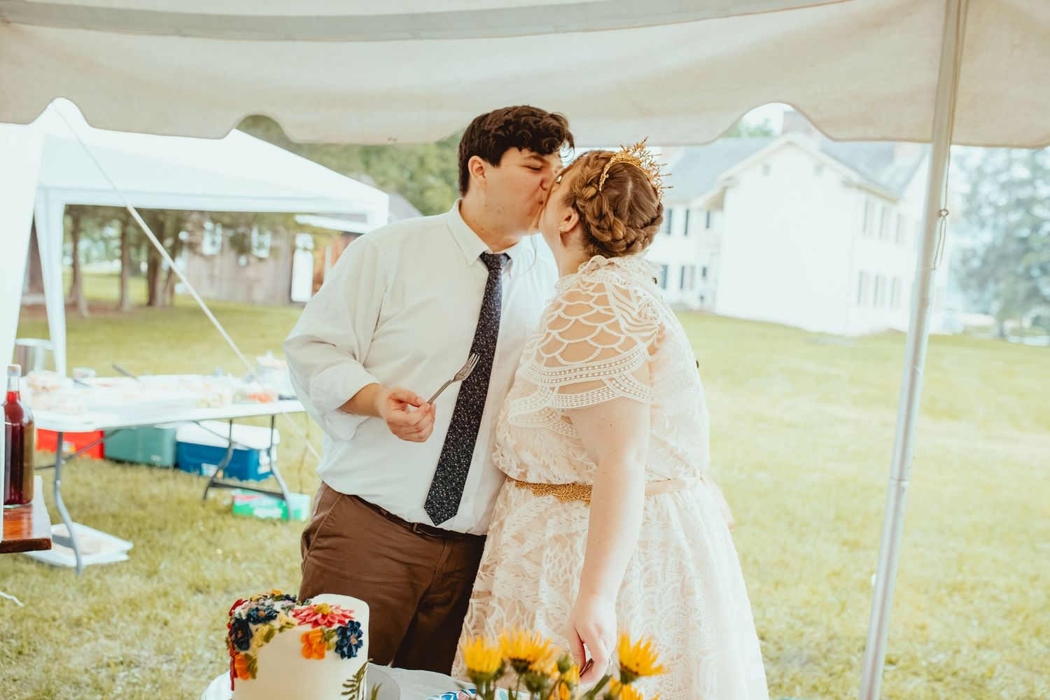 A couple cuts their wedding cake together at an outdoor reception under a white tent.