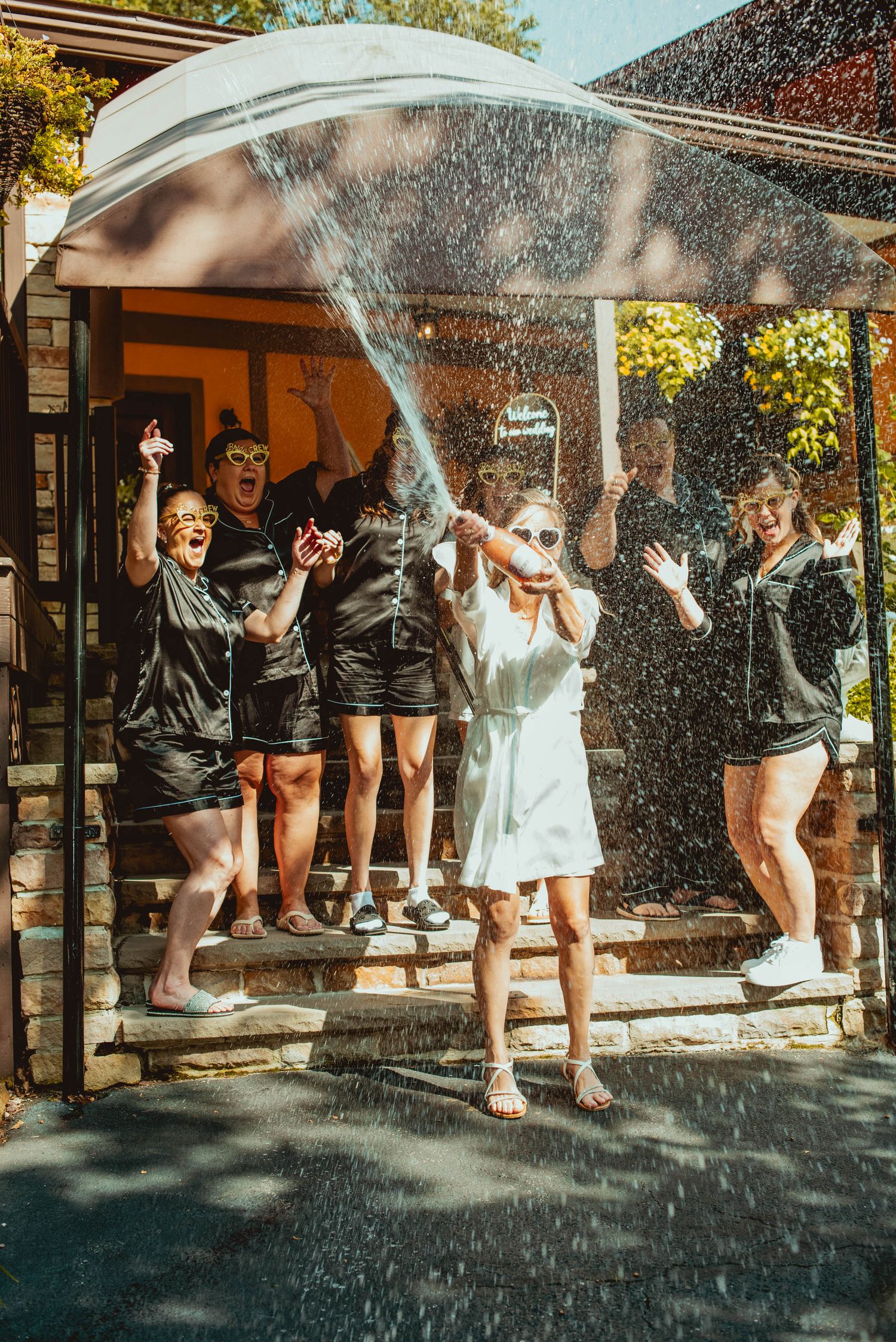 A group in black outfits and sunglasses splashes water during an outdoor celebration.