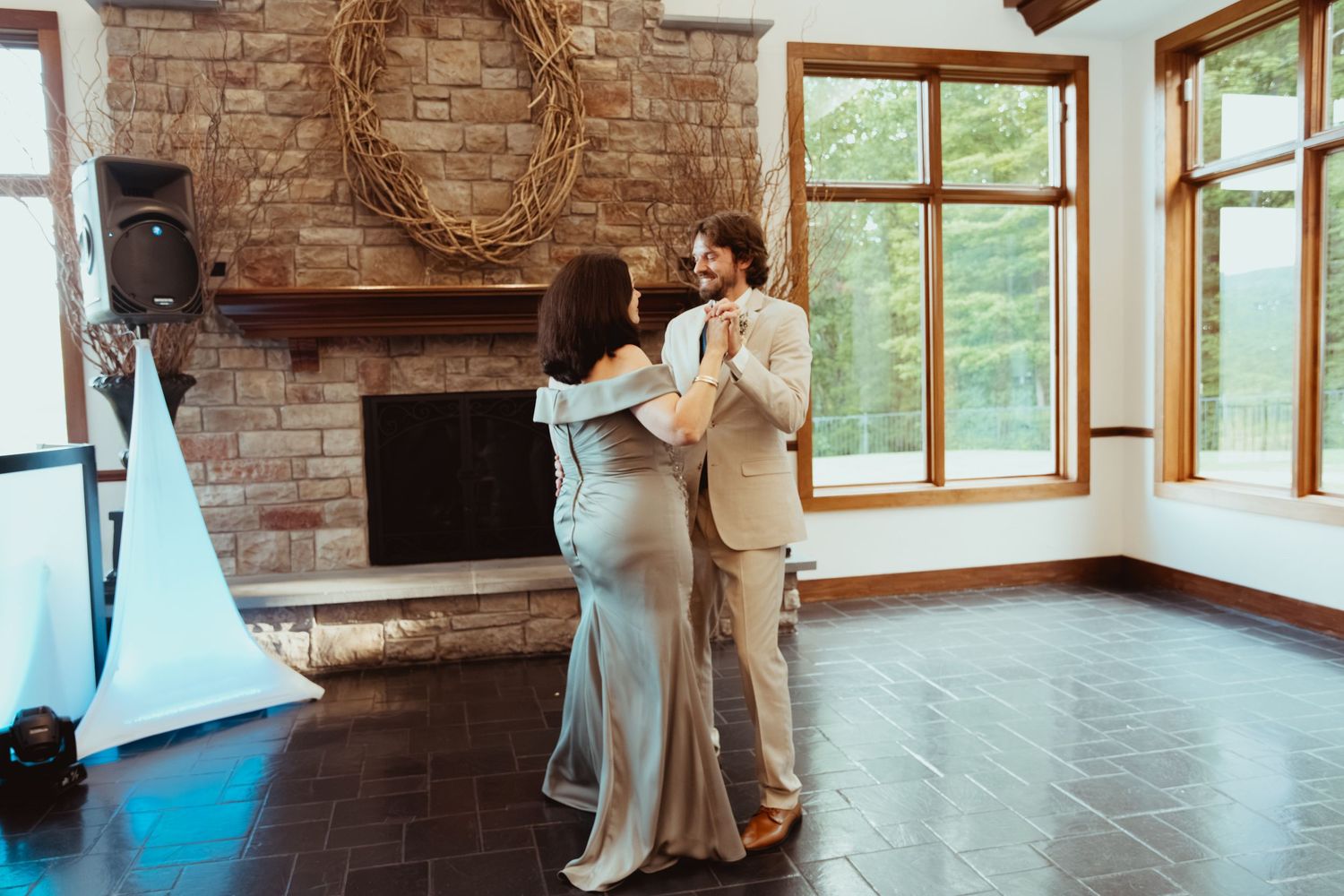 Couple sharing a romantic dance in an elegant venue with stone fireplace and large windows.