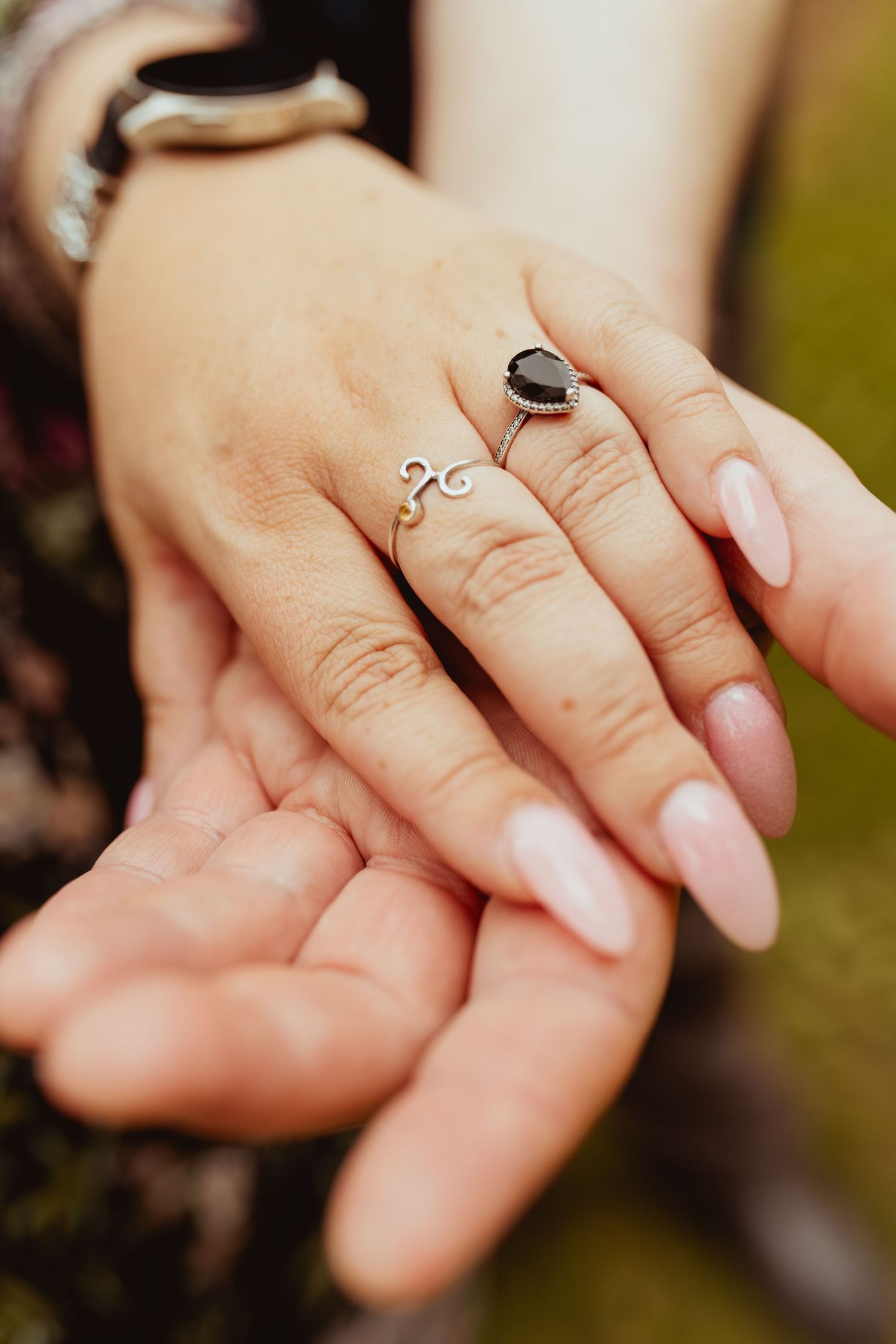 Close-up of two hands touching, woman wearing a delicate silver ring with black stone.