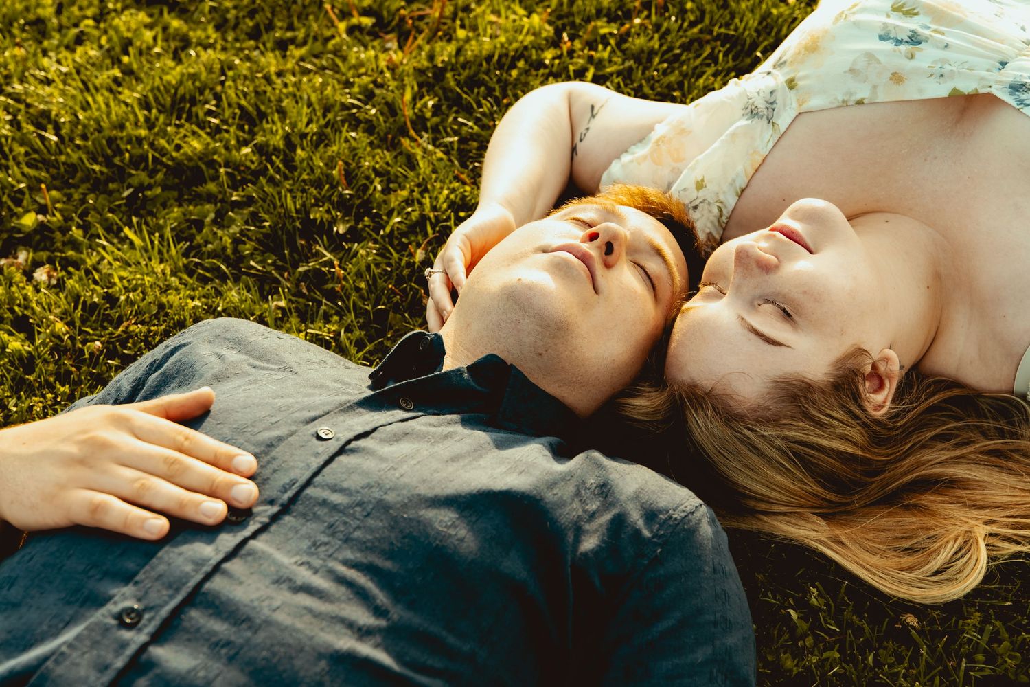 A romantic couple lying on green grass together, eyes closed, sharing a peaceful and intimate moment outdoors.