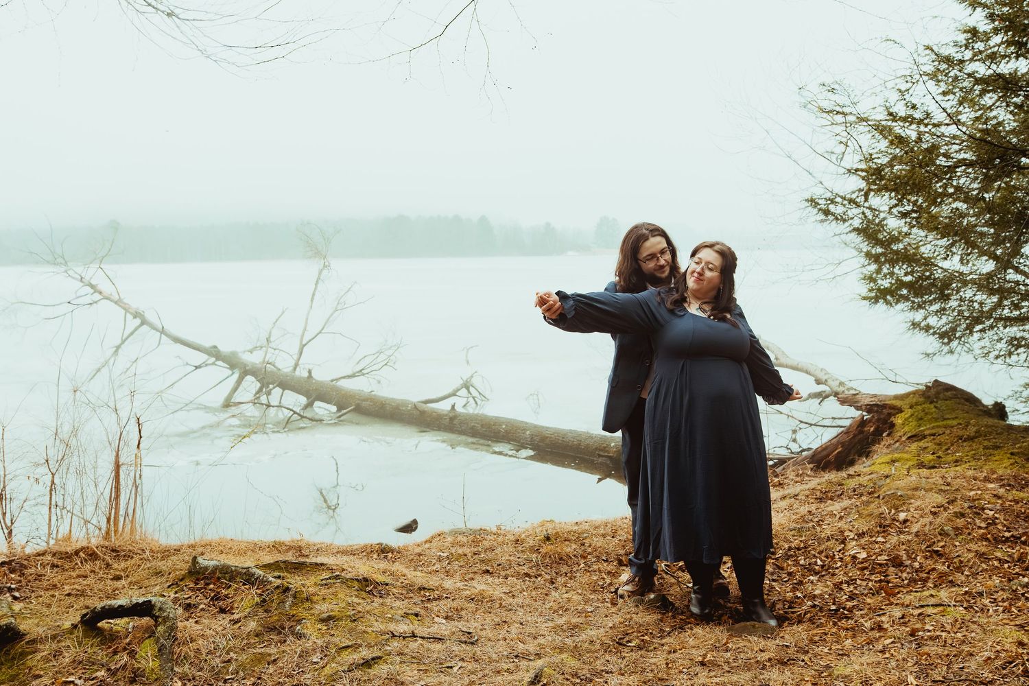 Friends enjoy a playful moment together on a scenic lakeside cliff during an overcast day.