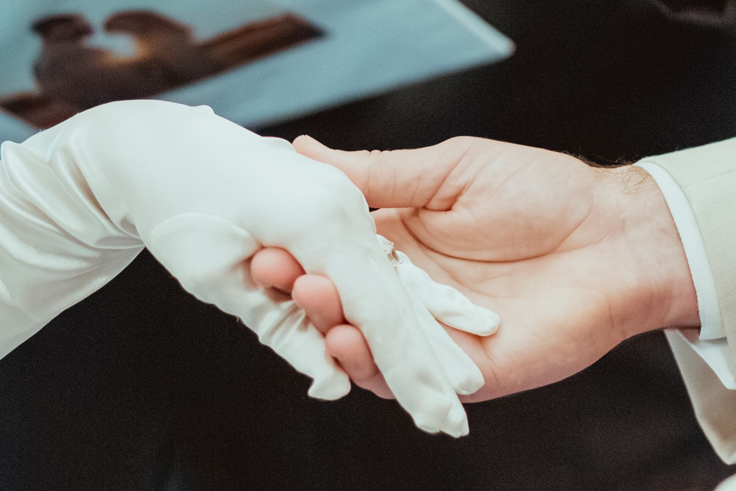 Two hands passing a white cloth napkin in a restaurant setting with dark background lighting.