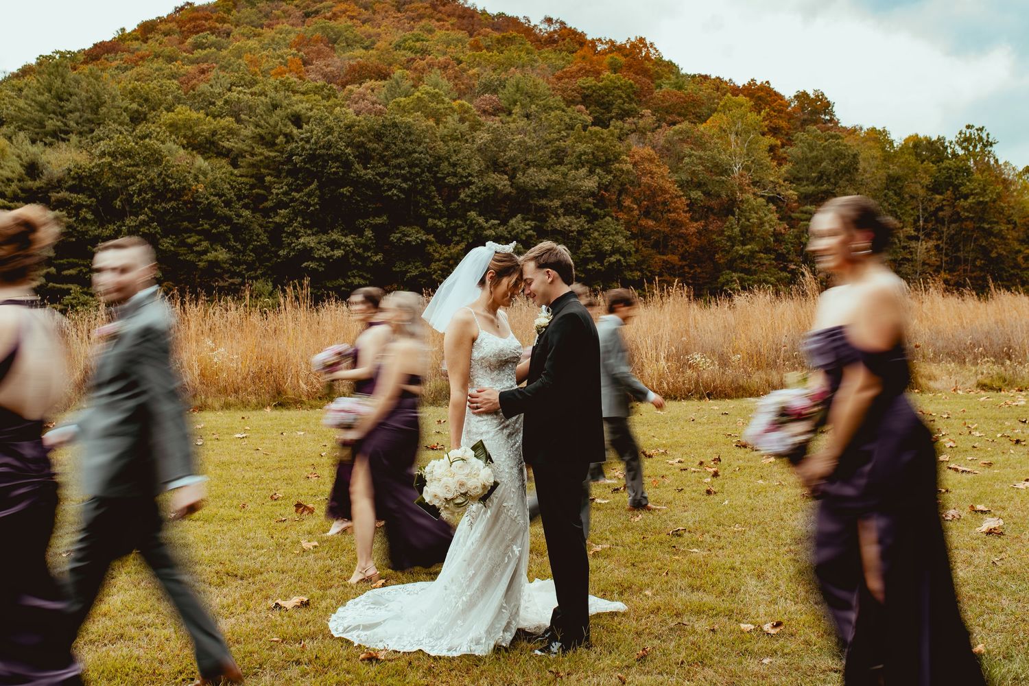 Wedding party dancing in field with mountain backdrop during fall season.