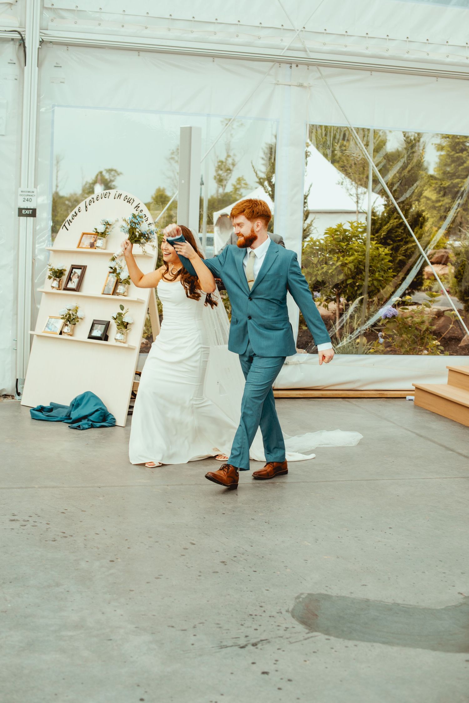 Wedding party dancing and celebrating on a concrete floor under a white tent.