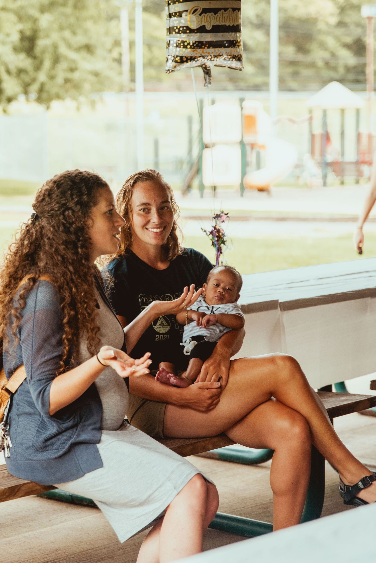 Two friends sit together on a covered porch sharing snacks and laughing during a casual outdoor hangout.