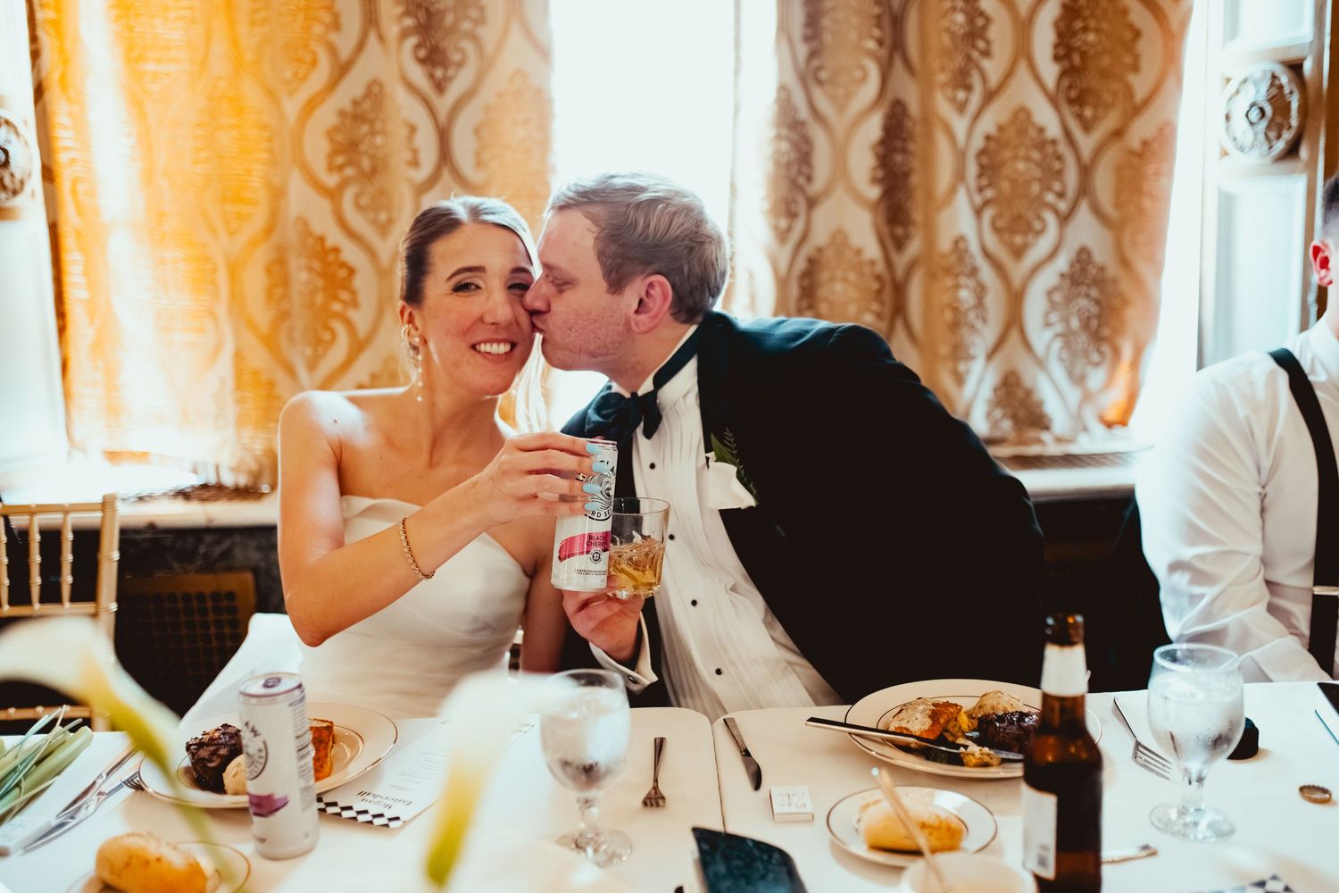 A joyful wedding celebration moment with champagne toasts at an elegant reception with golden curtains in the background.