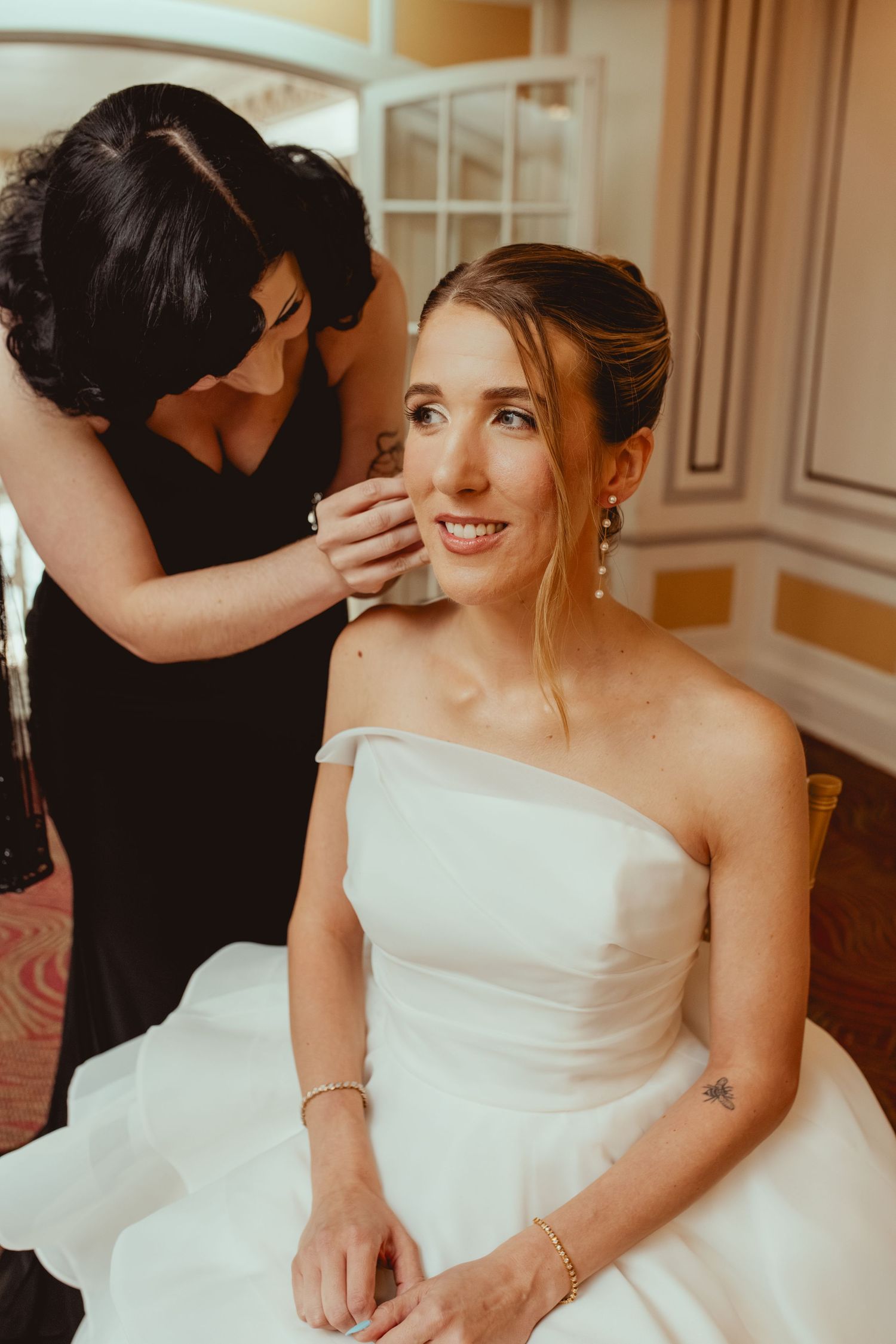 Bridesmaids in black dresses help adjust a white wedding gown before the ceremony.