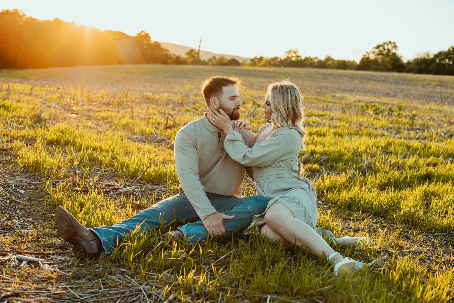 Couple lounges together on grassy hillside during golden sunset photography session.