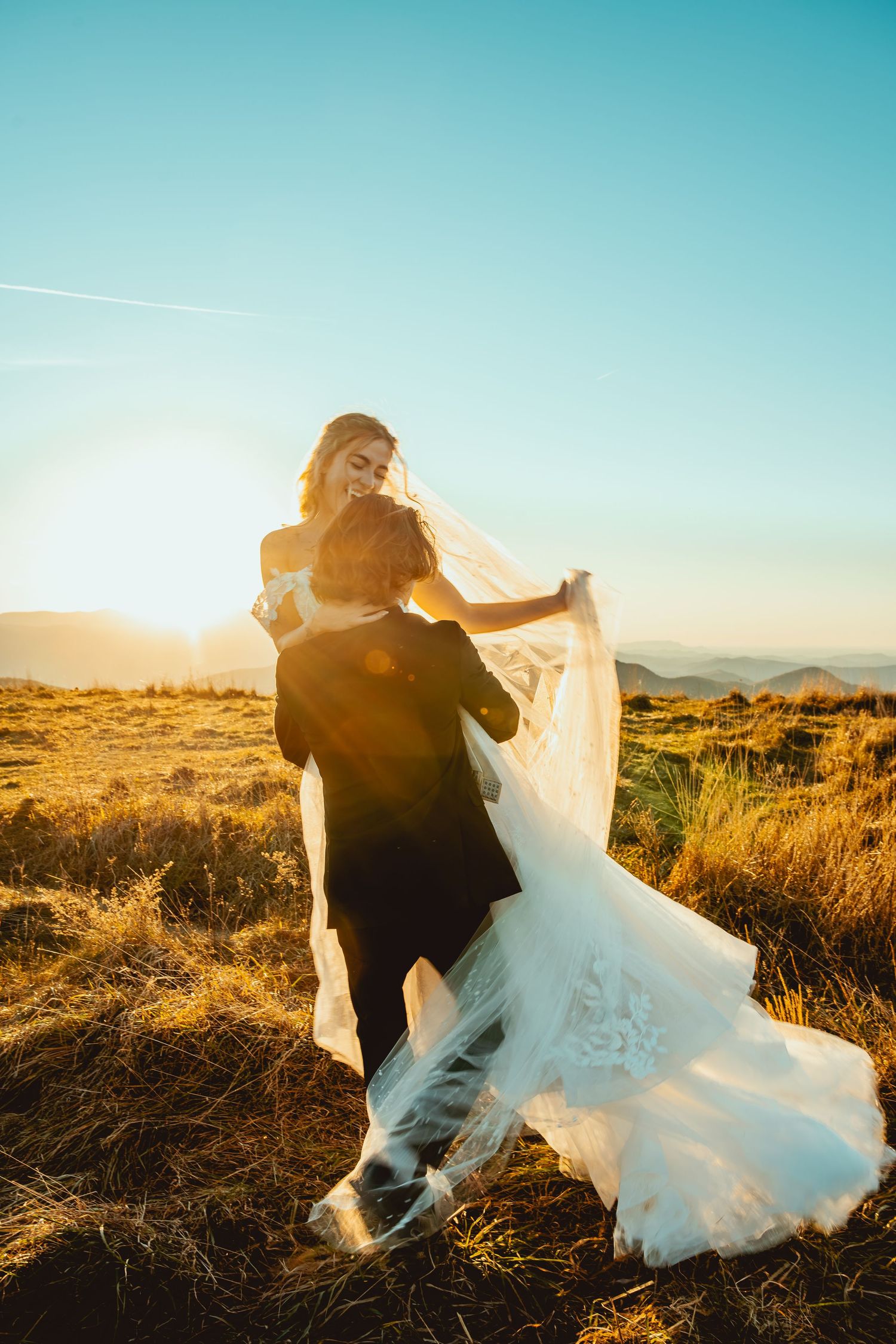 A couple dances in a desert field during sunset with the bride's dress flowing in the wind.