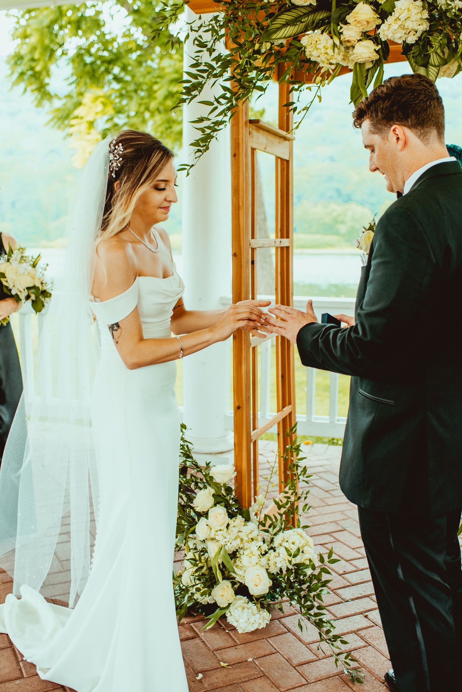 Couple exchanging rings during outdoor wedding ceremony with white floral decorations.
