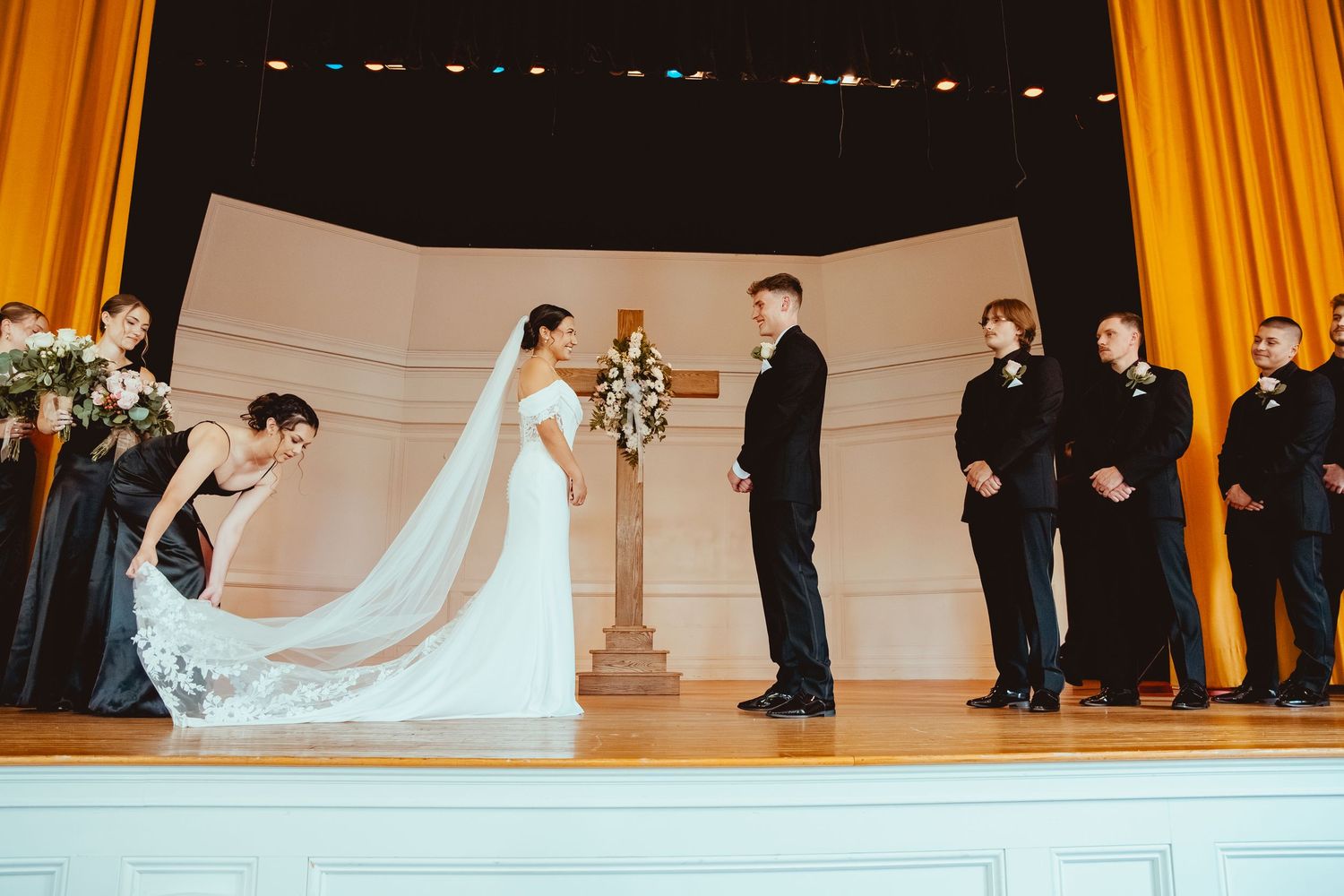 Wedding ceremony scene with golden curtains and white decor in an elegant indoor venue.