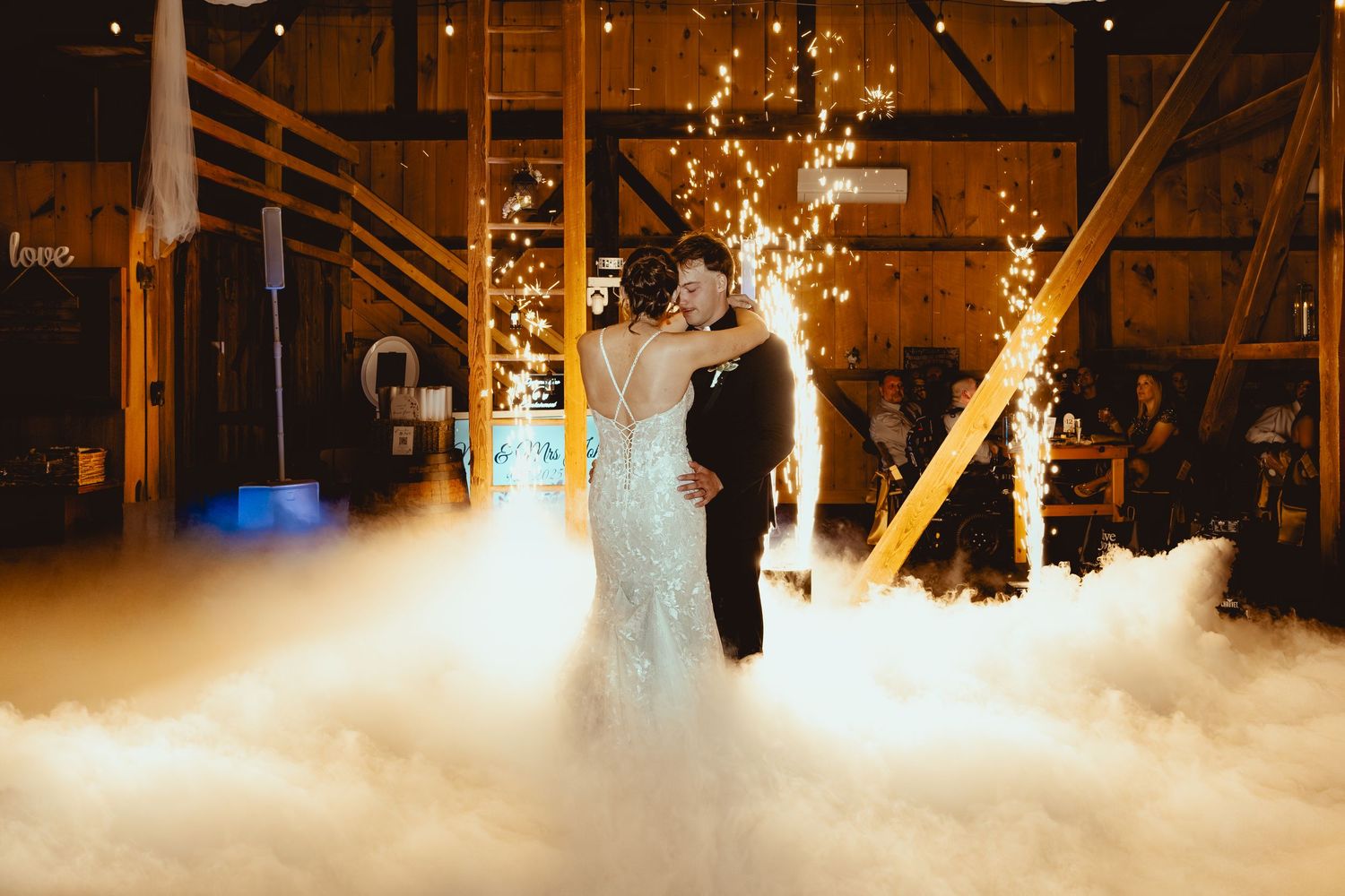 Wedding couple dancing on misty dance floor with dramatic lighting effects in barn venue.