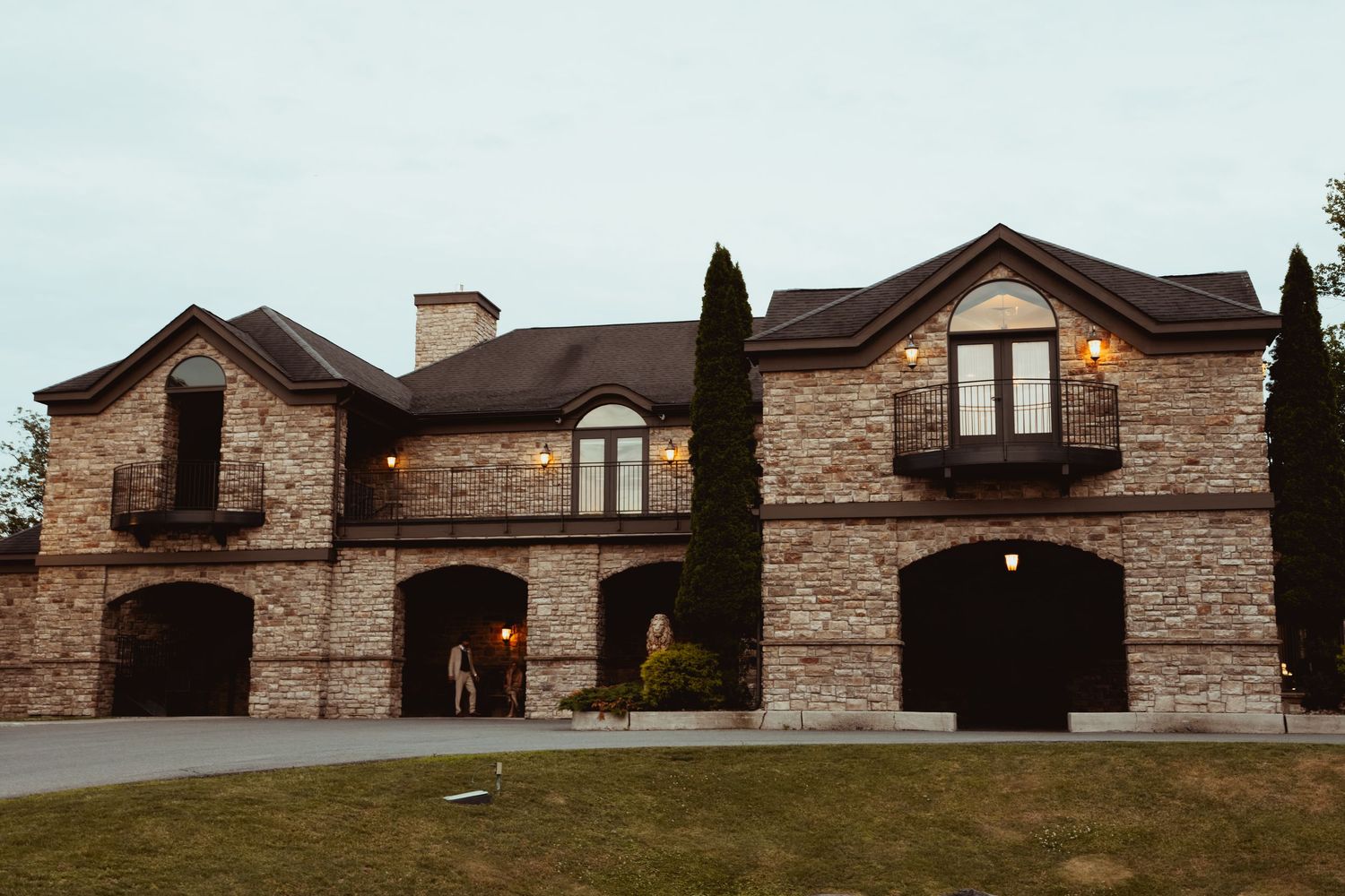 Grand brick wedding venue exterior with arched windows, balconies, and cypress trees at dusk.