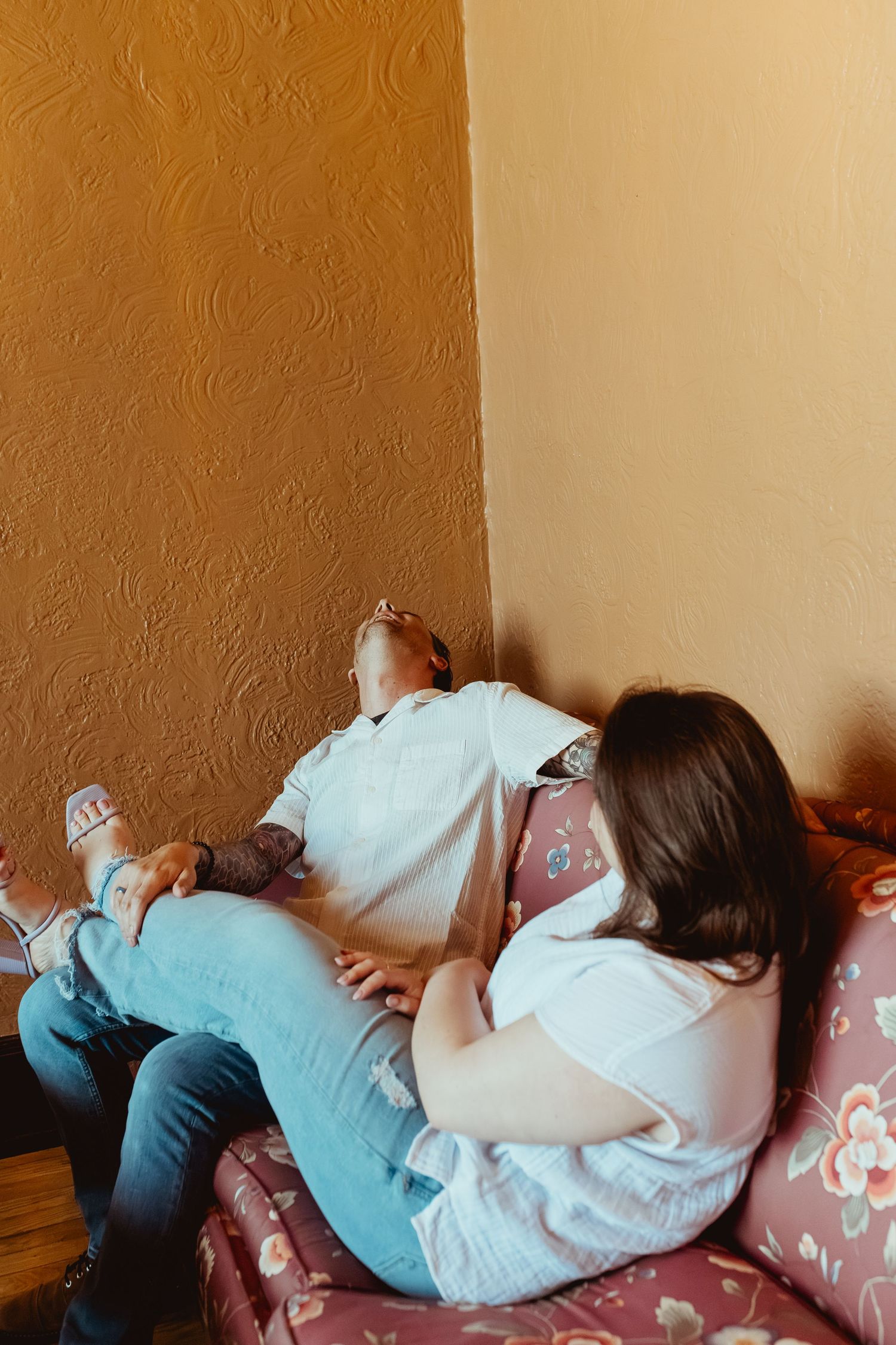 Couple relaxing together on a floral sofa in a cozy room with textured walls.