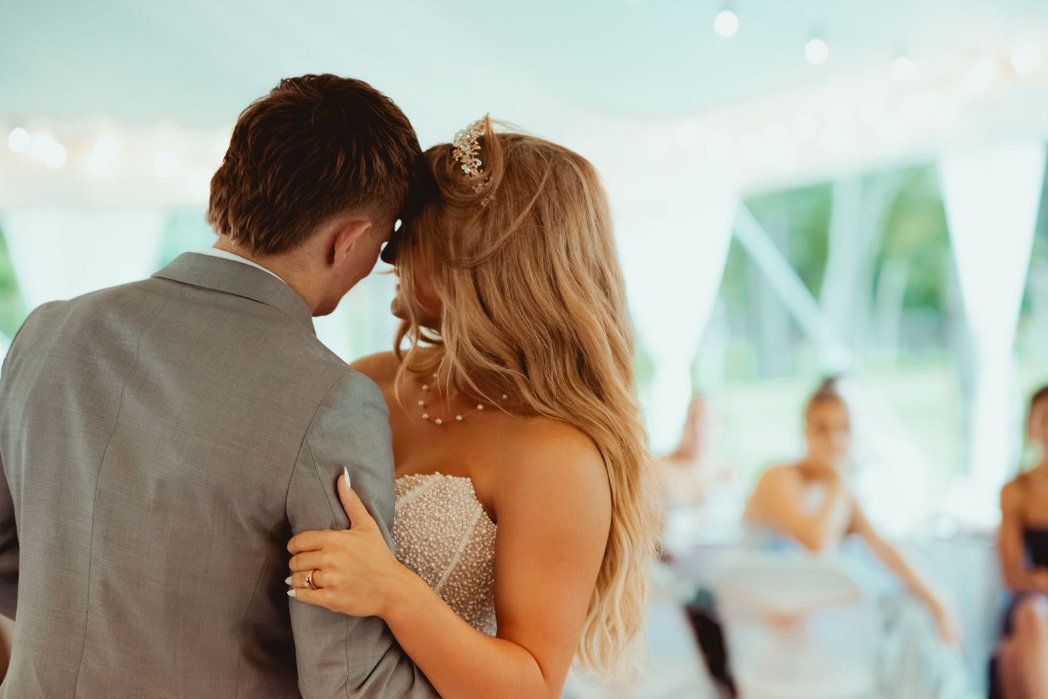 Bride and groom share intimate first dance moment under twinkling lights at wedding reception.