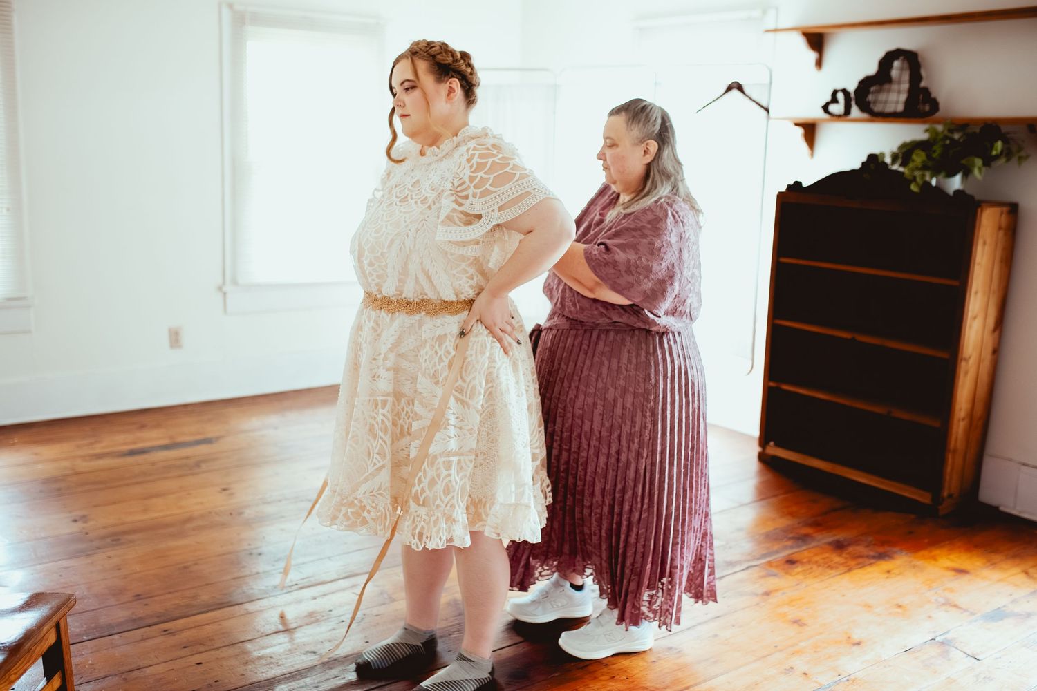 Two people dancing together on a wooden floor in vintage-style dresses during a special occasion.