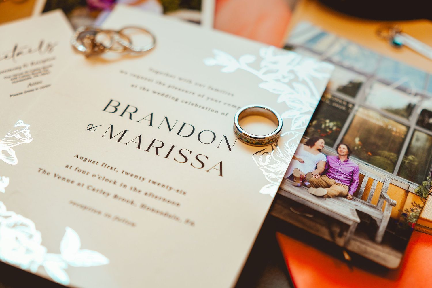 Wedding invitation for Brandon and Marissa with gold rings resting on top, surrounded by photos and stationery details.