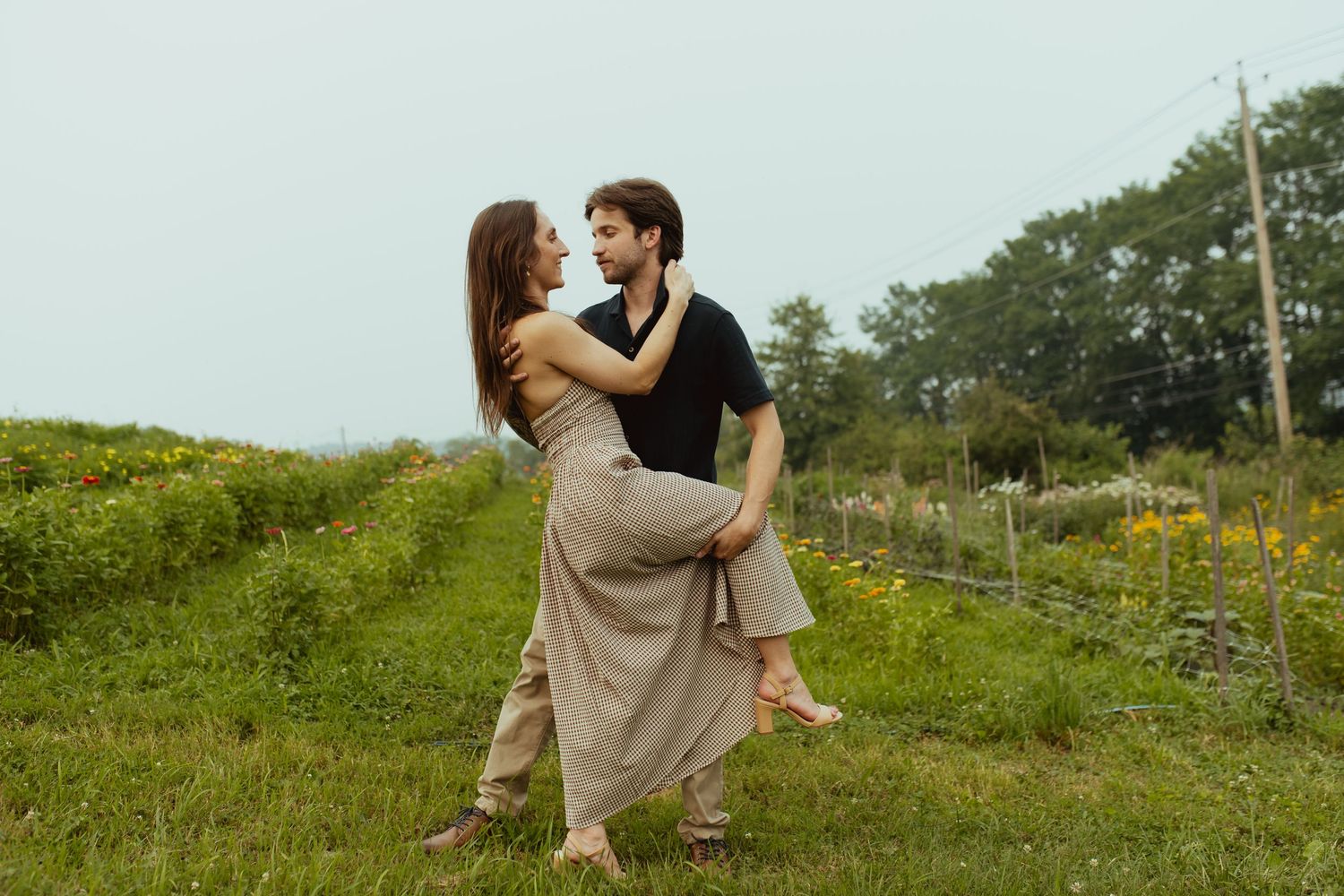 Couple dancing romantically in a lush green garden, woman in flowing beige dress, man in black shirt, surrounded by wildflowers.