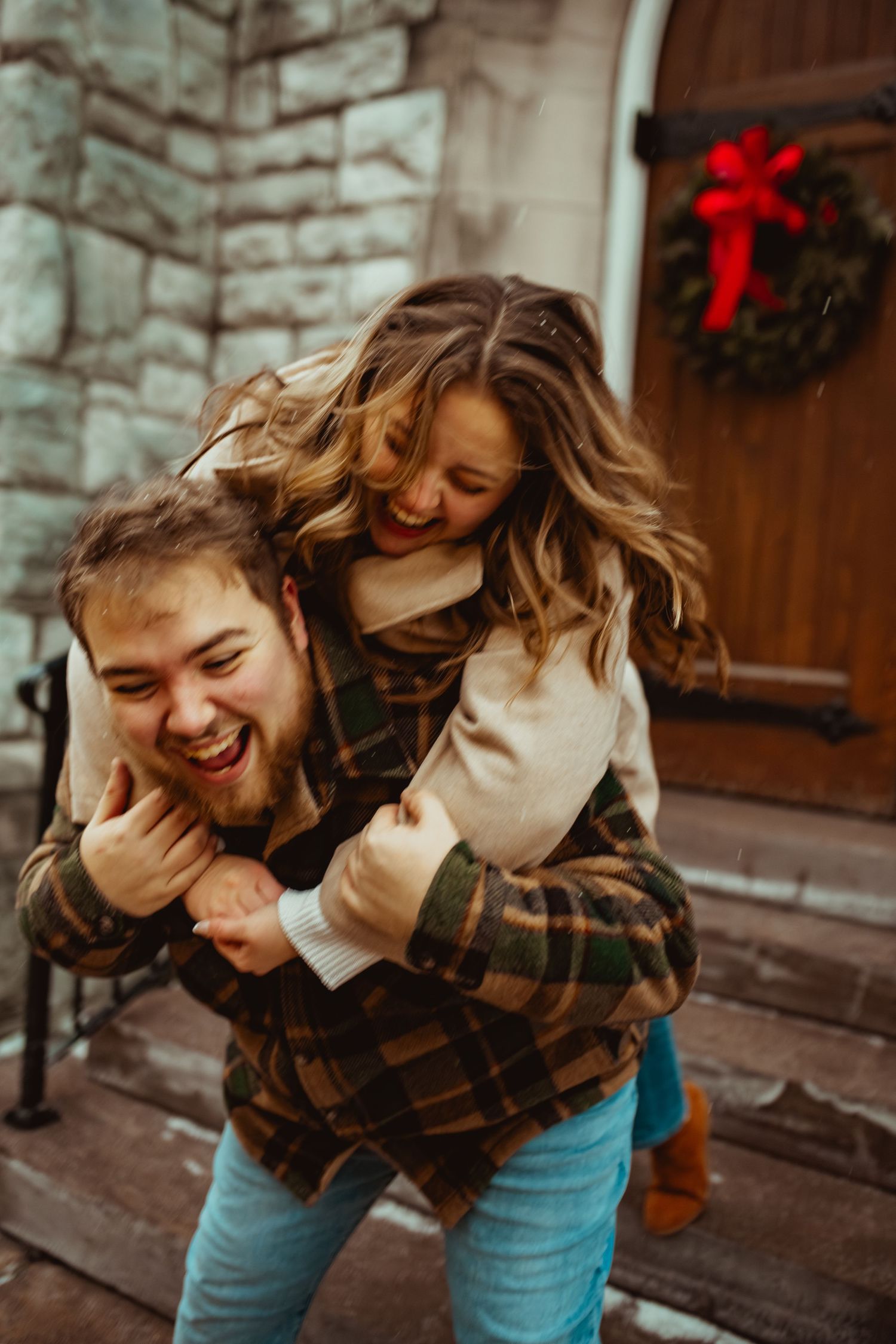 A playful moment captured between two people near a stone wall with holiday decorations.