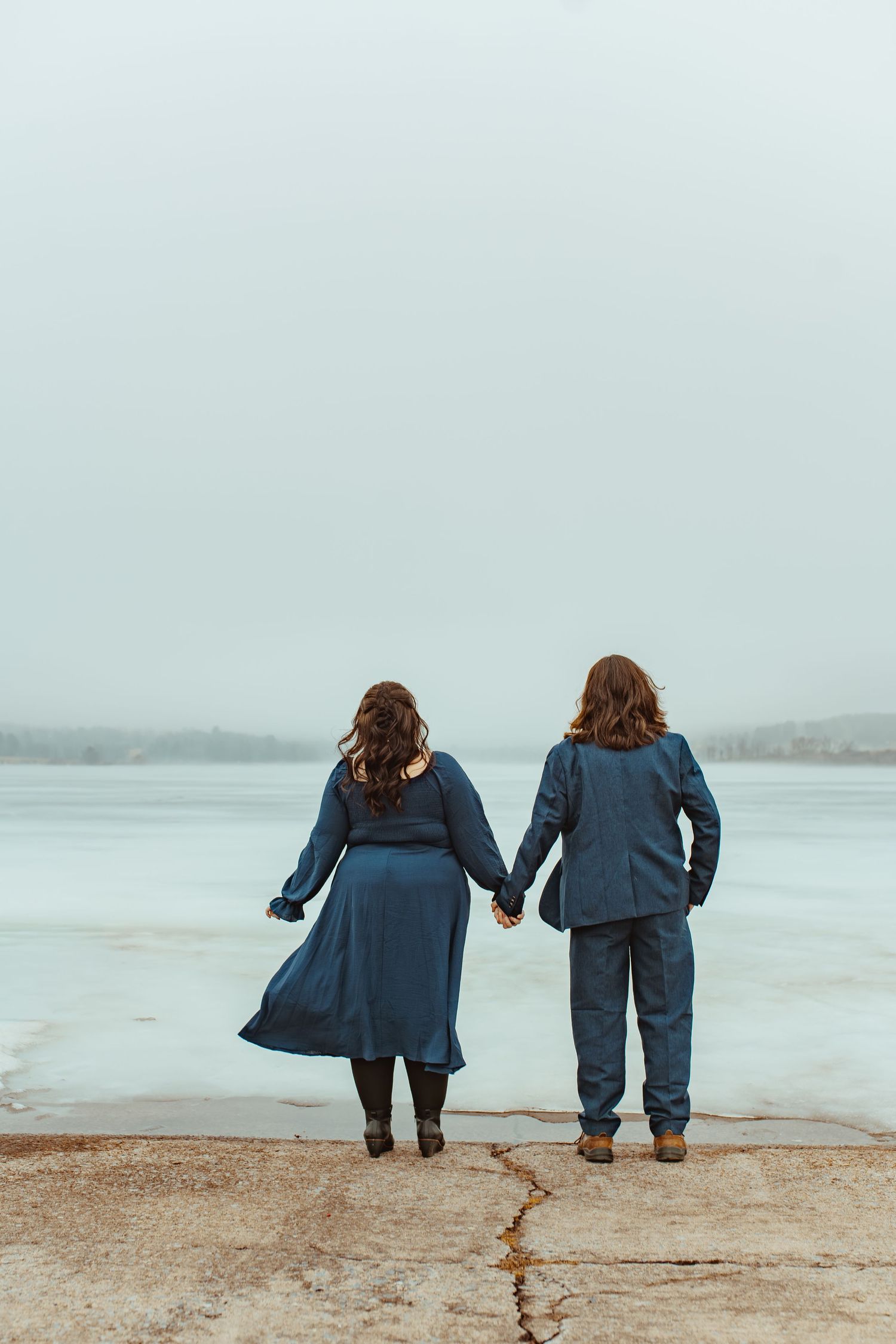 Two people in denim outfits walk along a misty beach shoreline in a series of progressive shots.