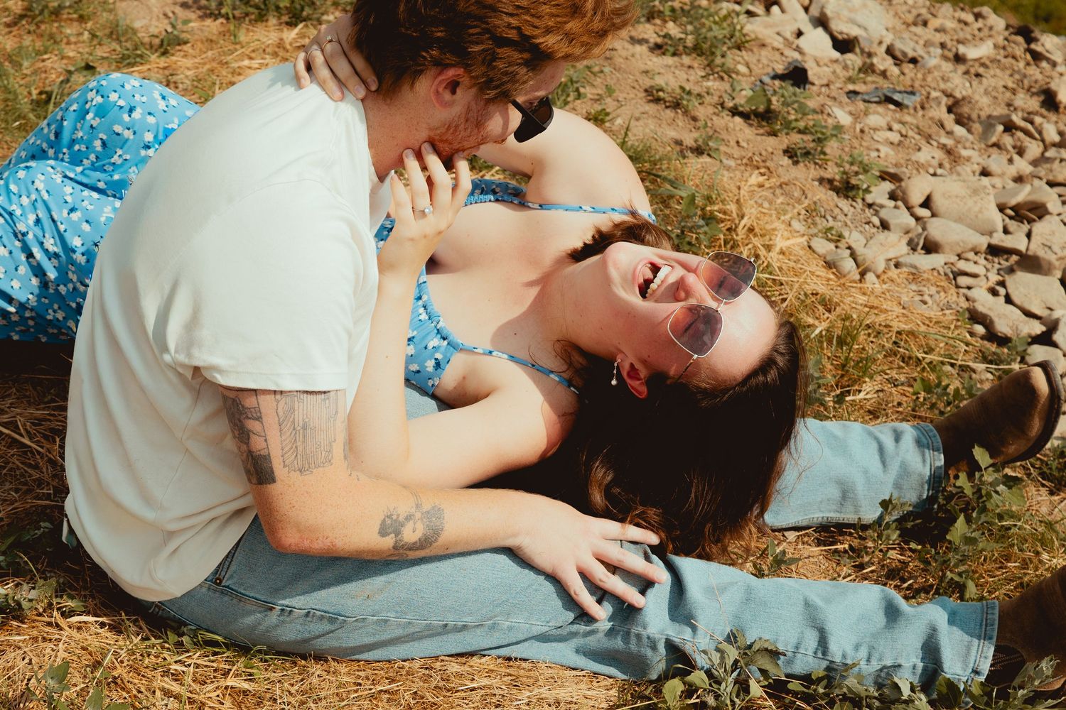 A person gently petting a small grey kitten on rocky ground in warm sunlight.