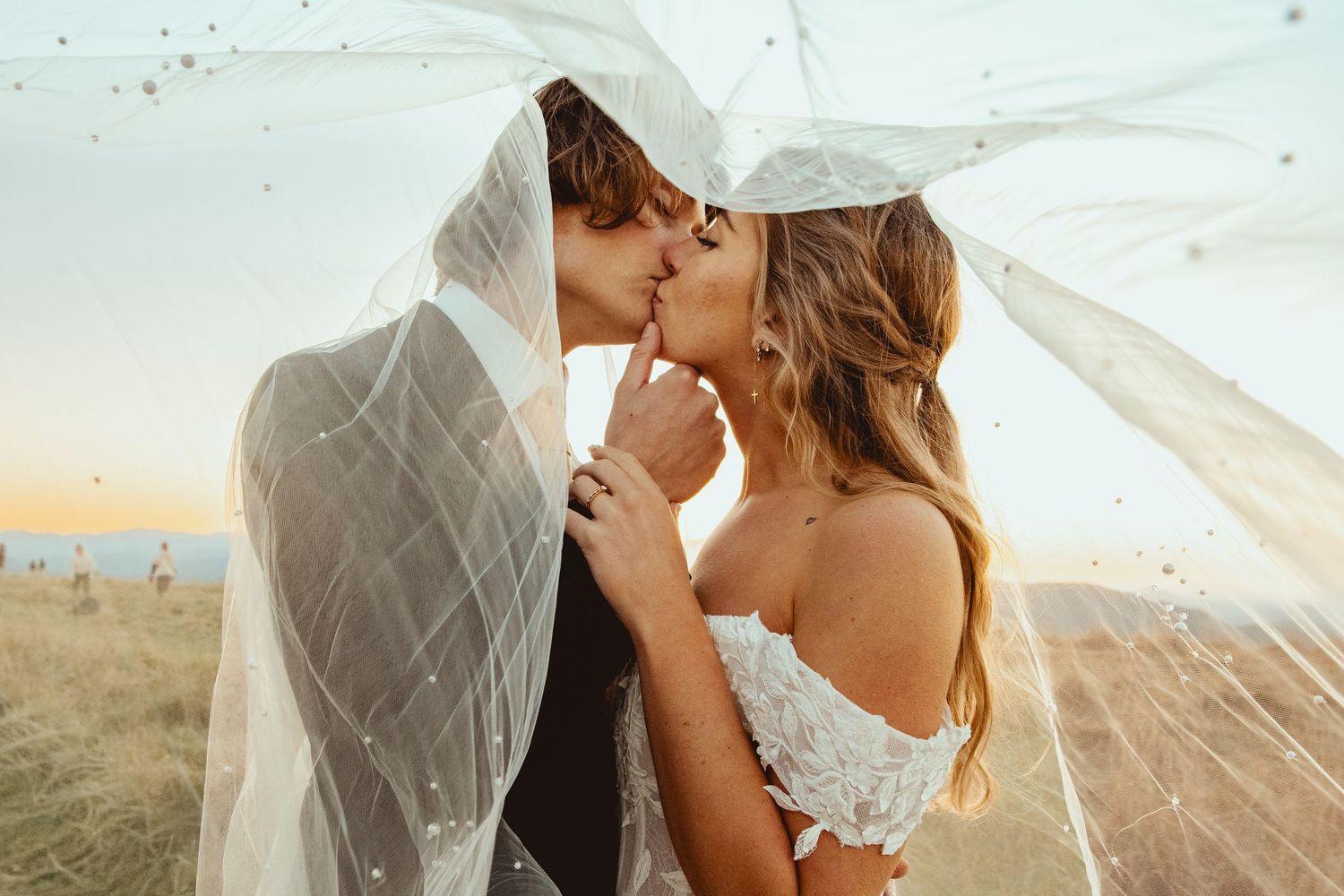 A romantic wedding kiss captured through a flowing veil at sunset.