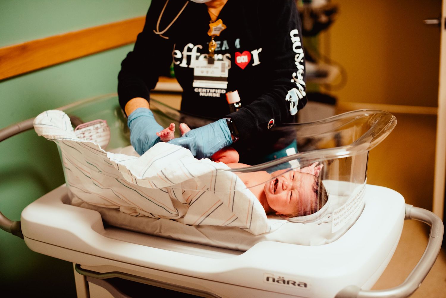 A healthcare worker in blue gloves examines a newborn baby lying on a medical examination table.