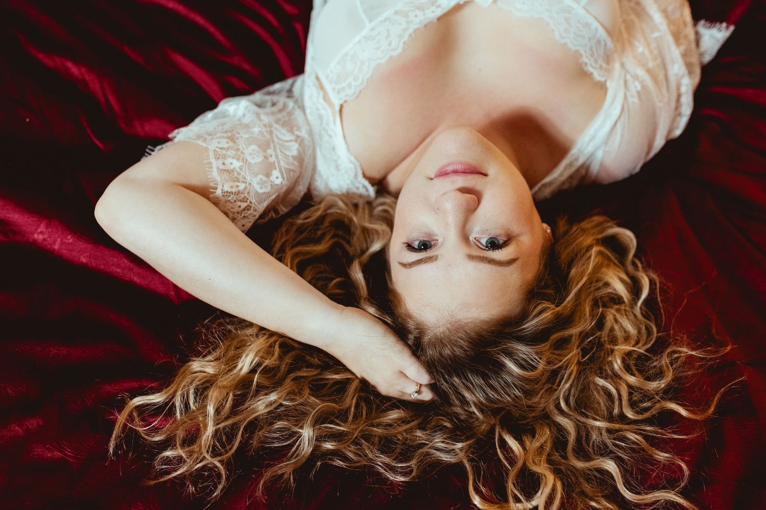 A romantic boudoir photo series with red velvet fabric and soft lighting shows a figure in delicate white lace.
