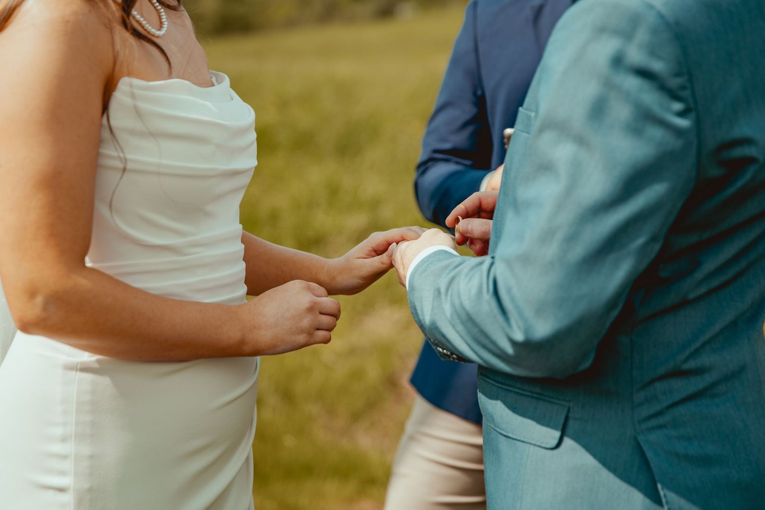 Close-up of wedding attire showing teal suits and white gowns during outdoor ceremony.
