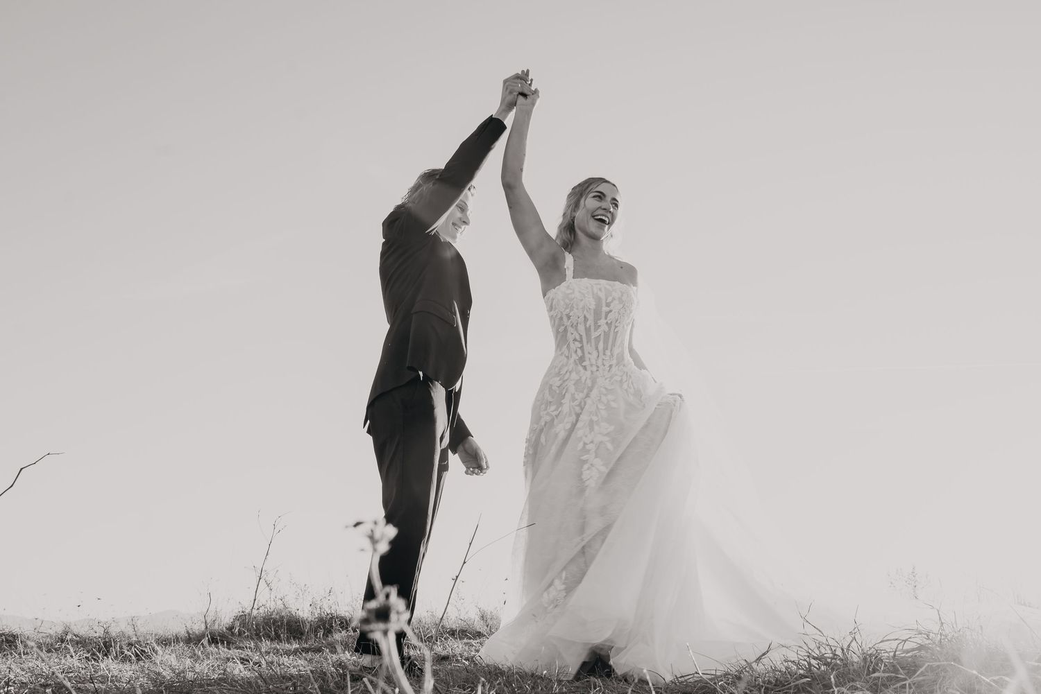 A black and white photo series shows a couple in wedding attire walking and dancing in a grassy field.