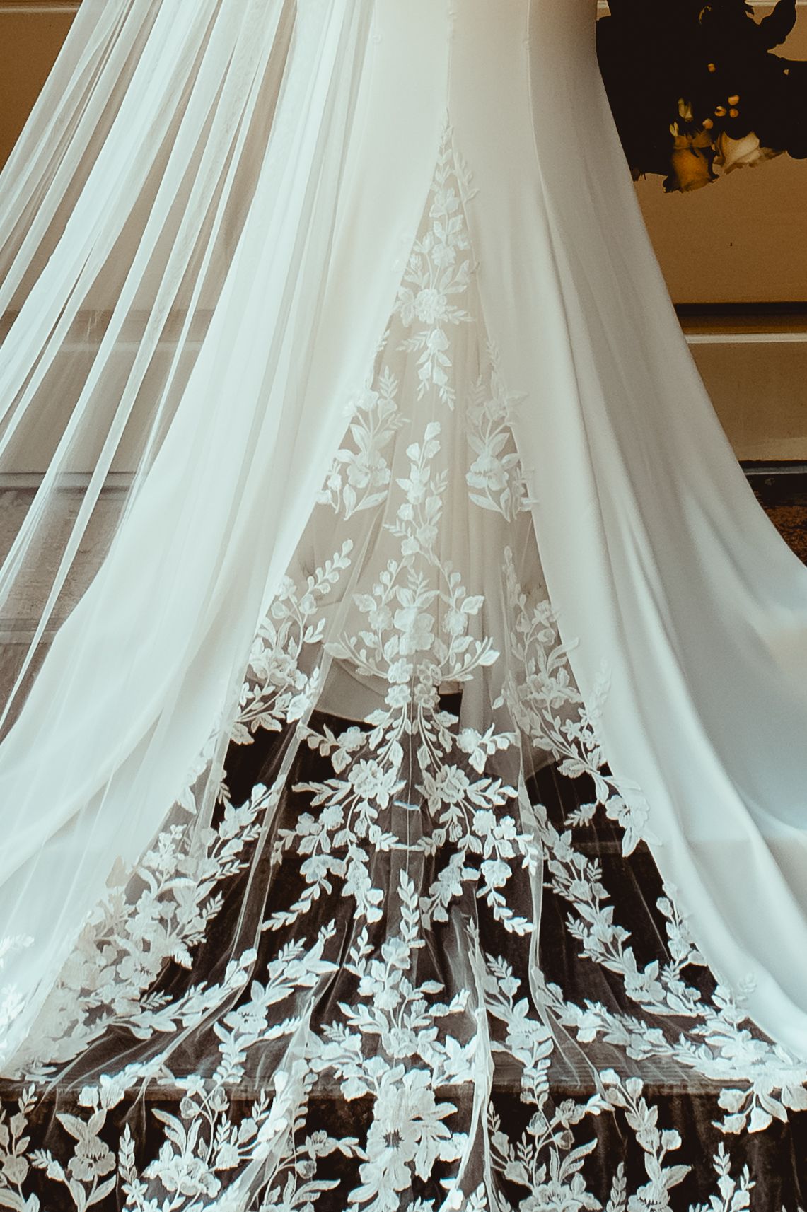 Delicate white lace butterflies and floral appliques adorn the hem of a flowing wedding dress veil.