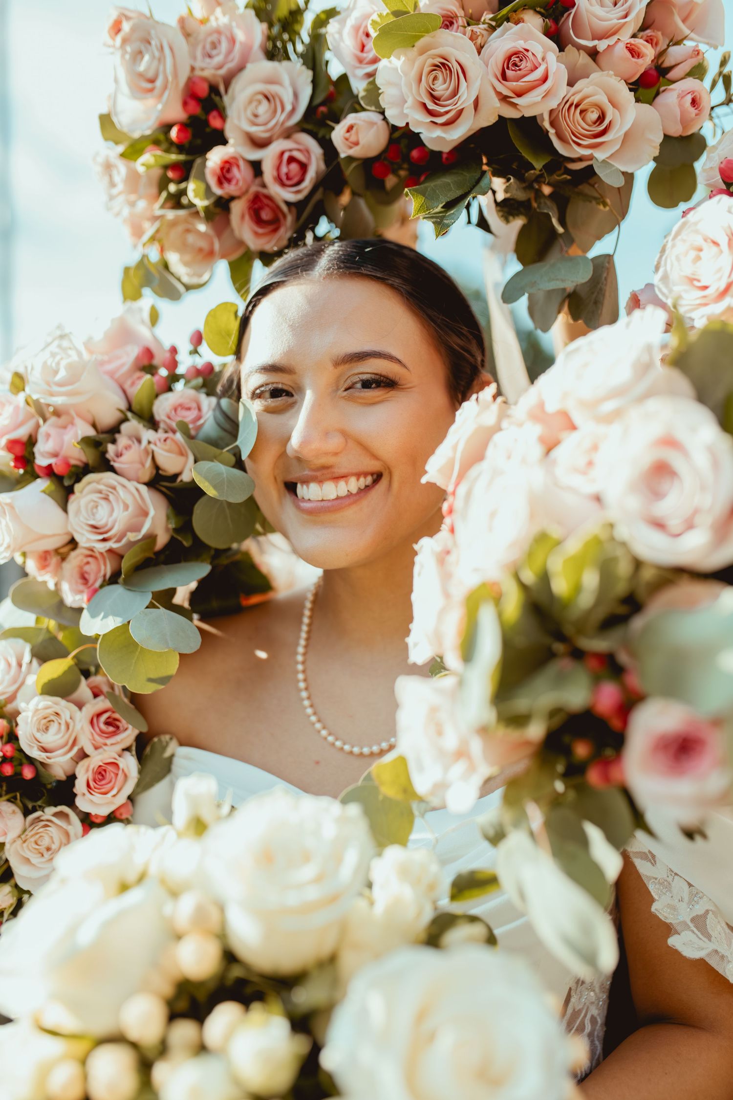 A romantic bridal portrait surrounded by blush pink roses and eucalyptus leaves in natural sunlight.