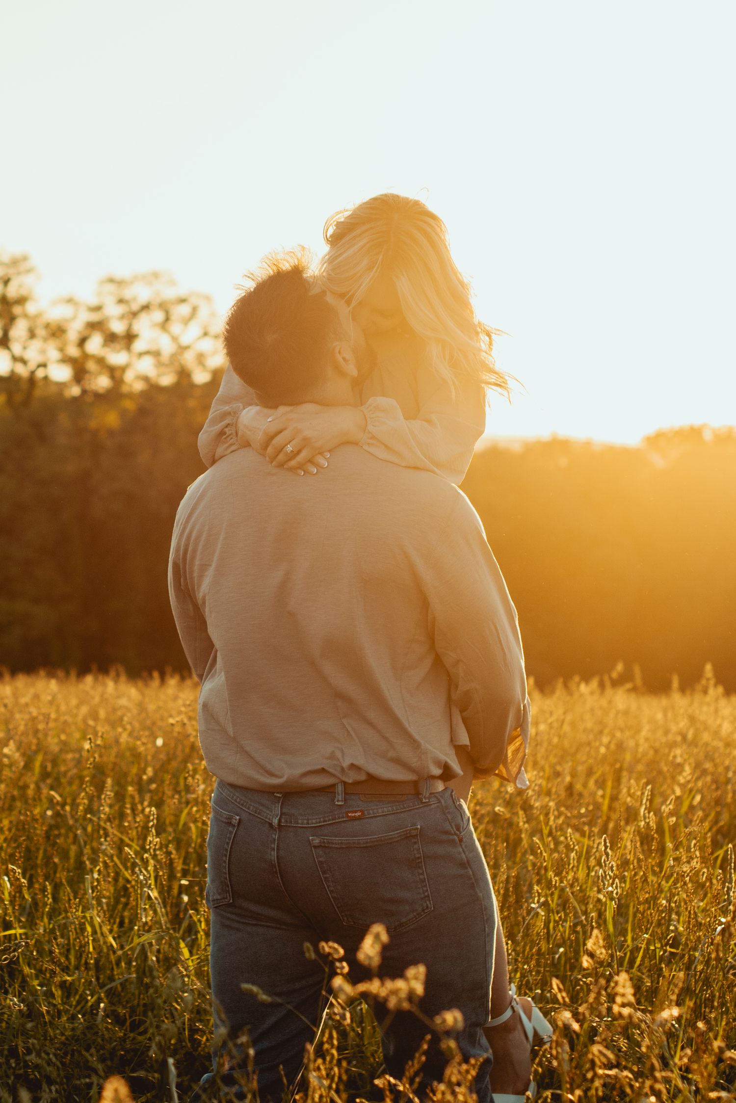 Intimate embrace captured in warm evening light amidst wildflower meadow.