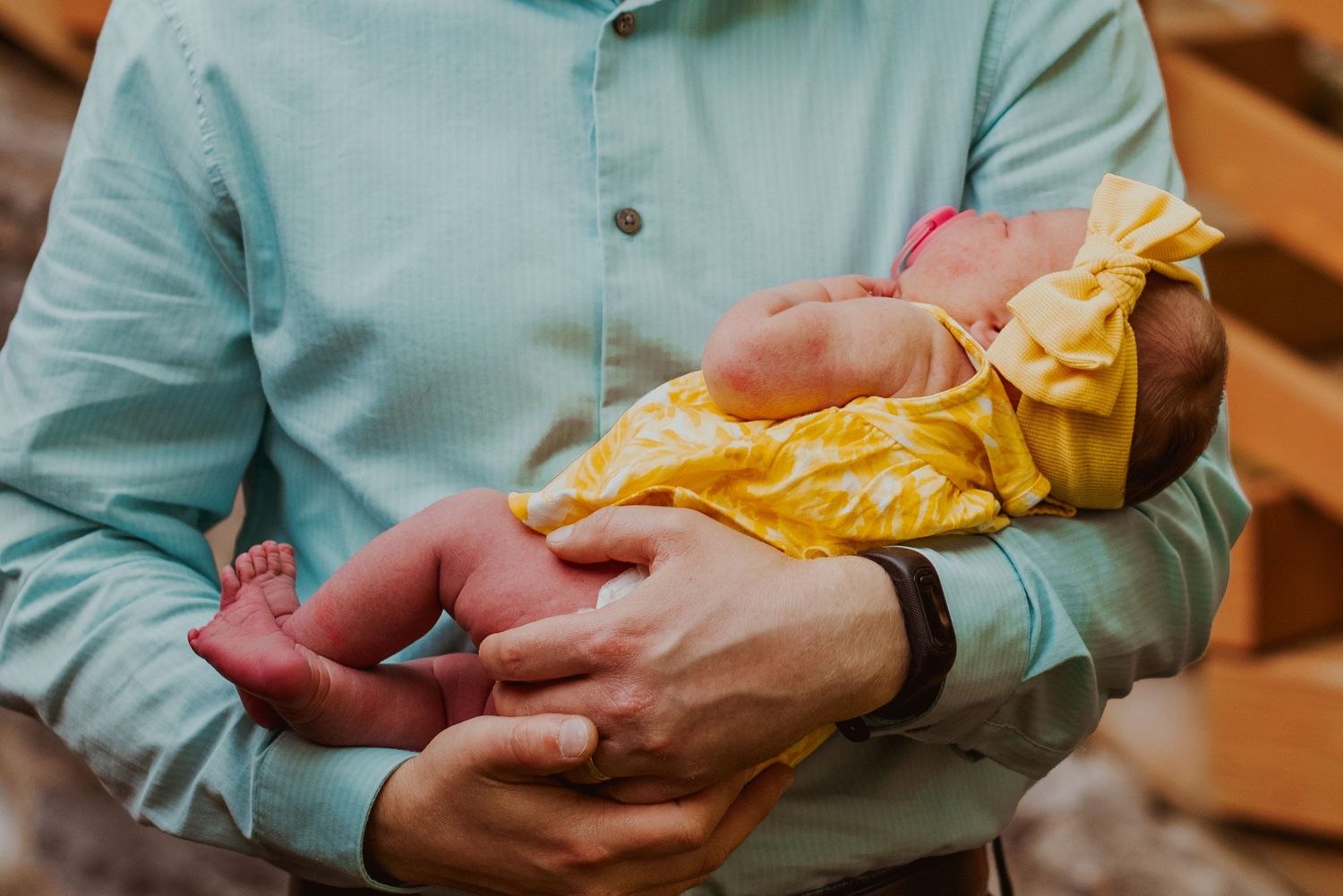 A newborn baby wrapped in a yellow swaddle blanket is held gently in arms wearing a mint green shirt.