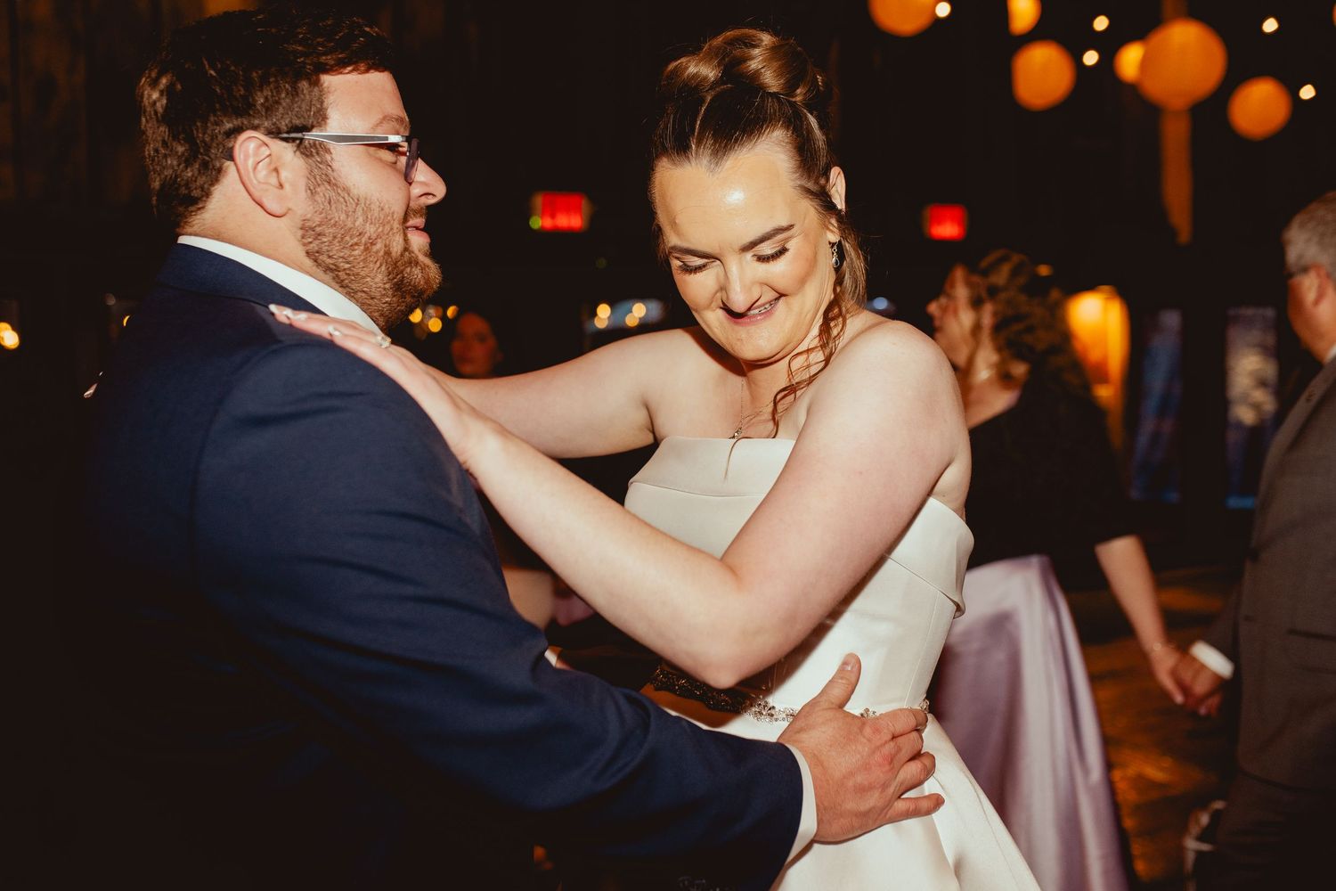 Bride and groom share a joyful first dance in a warmly lit reception venue.