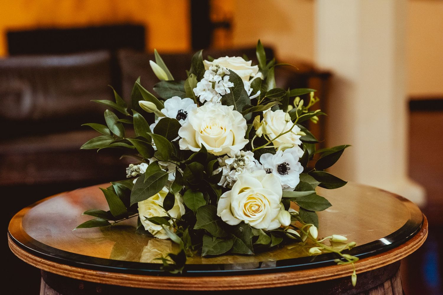 White roses and floral arrangements displayed on wooden tables with gold trim for an elegant wedding reception.