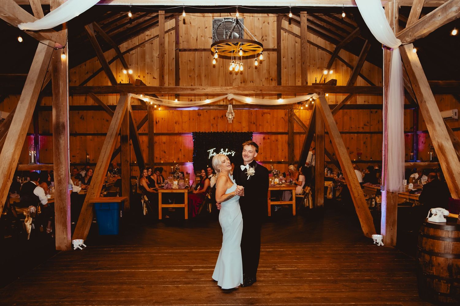 A rustic barn wedding venue decorated with white draping and string lights for an evening celebration.