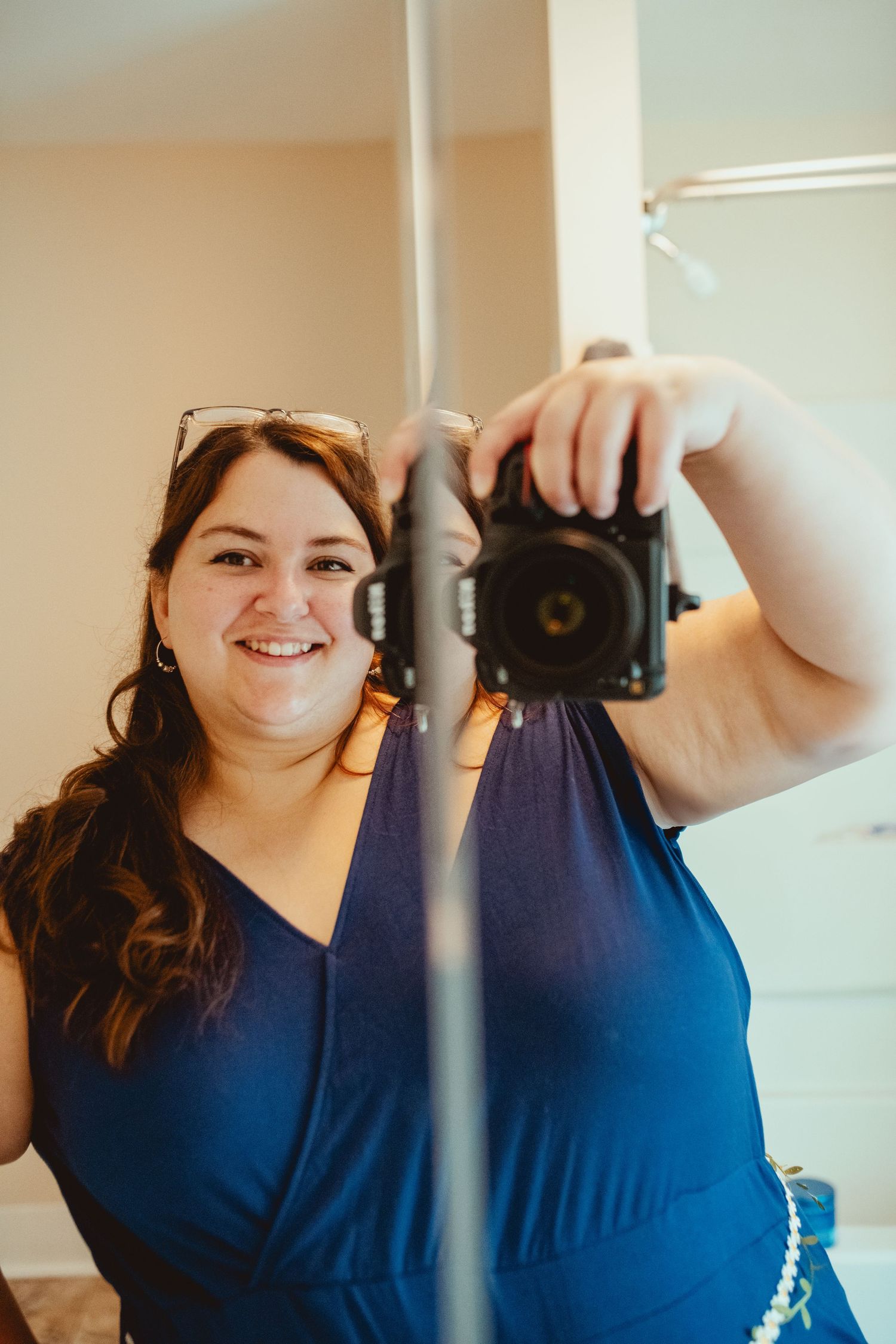 A photographer takes a mirror selfie with a camera while wearing a navy blue dress.