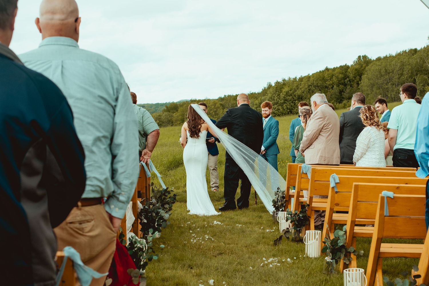 Rustic outdoor wedding ceremony with wooden bench seating and white door backdrop.