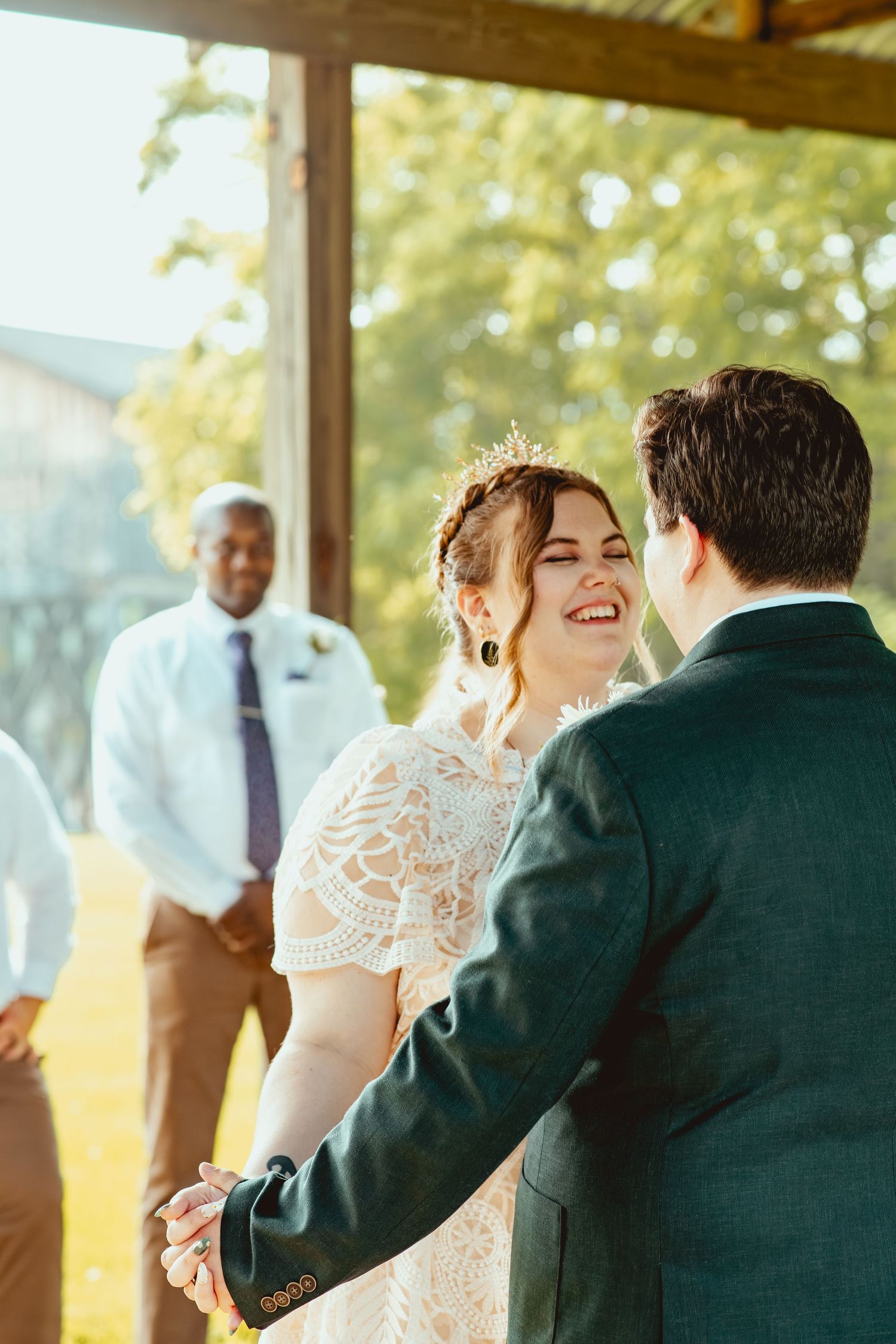 A joyful wedding couple shares a dance together at their outdoor reception in golden sunlight.