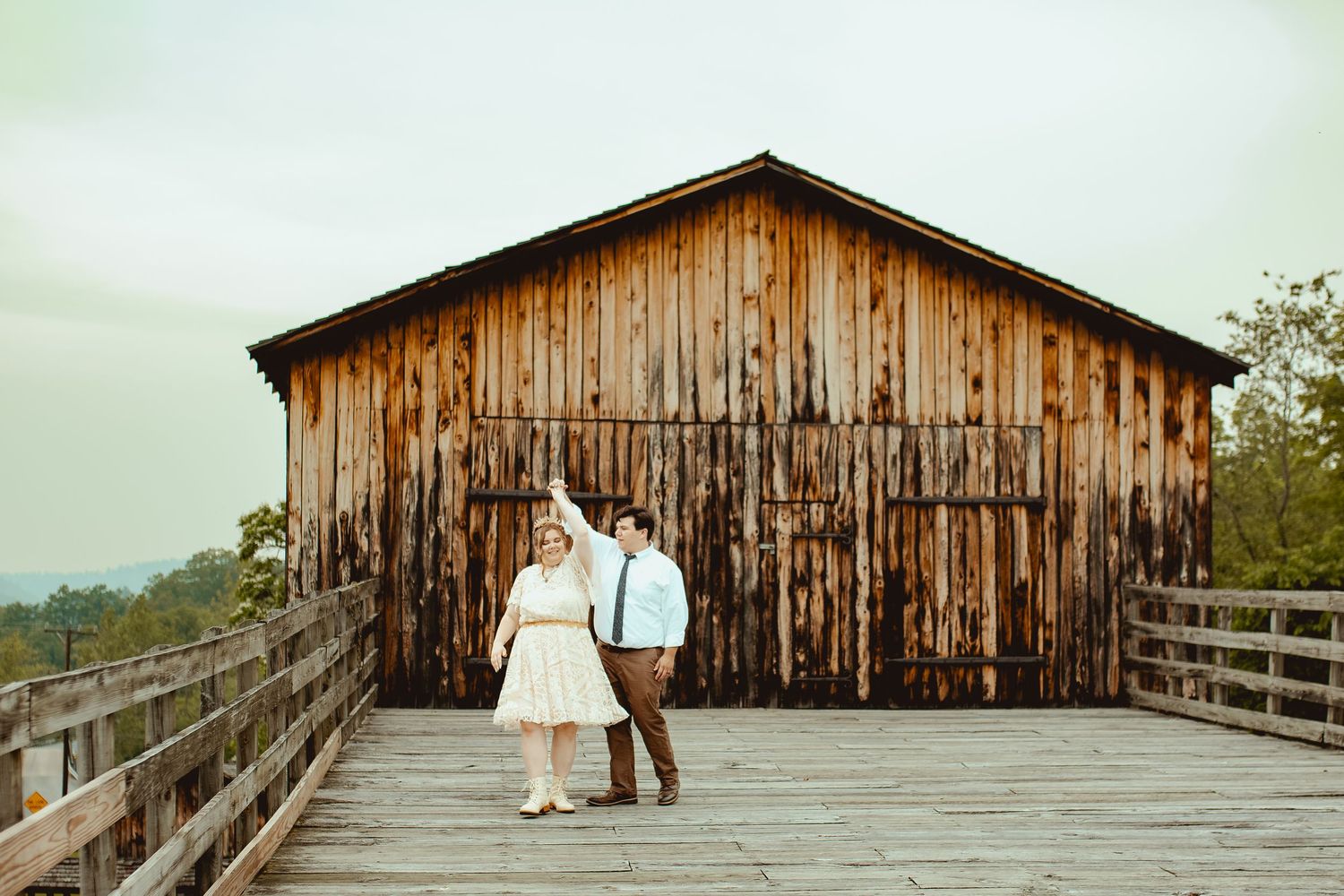 A rustic wooden barn with a long wooden boardwalk stretches across a serene landscape.