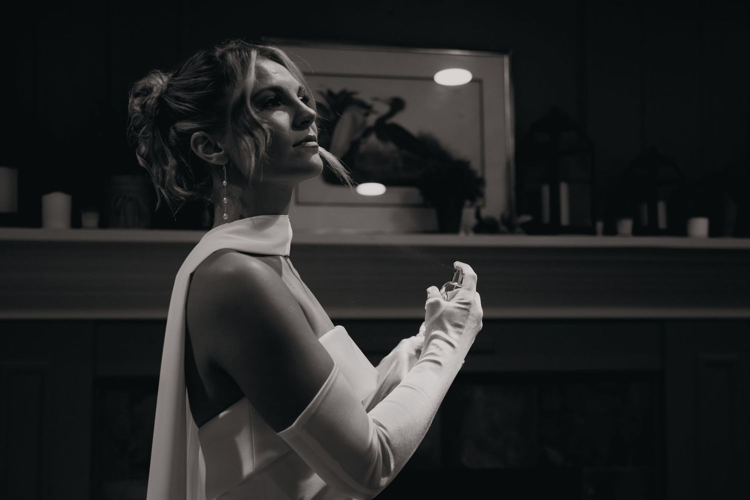 A person in a black dress poses dramatically in a dimly lit room with theatrical lighting.