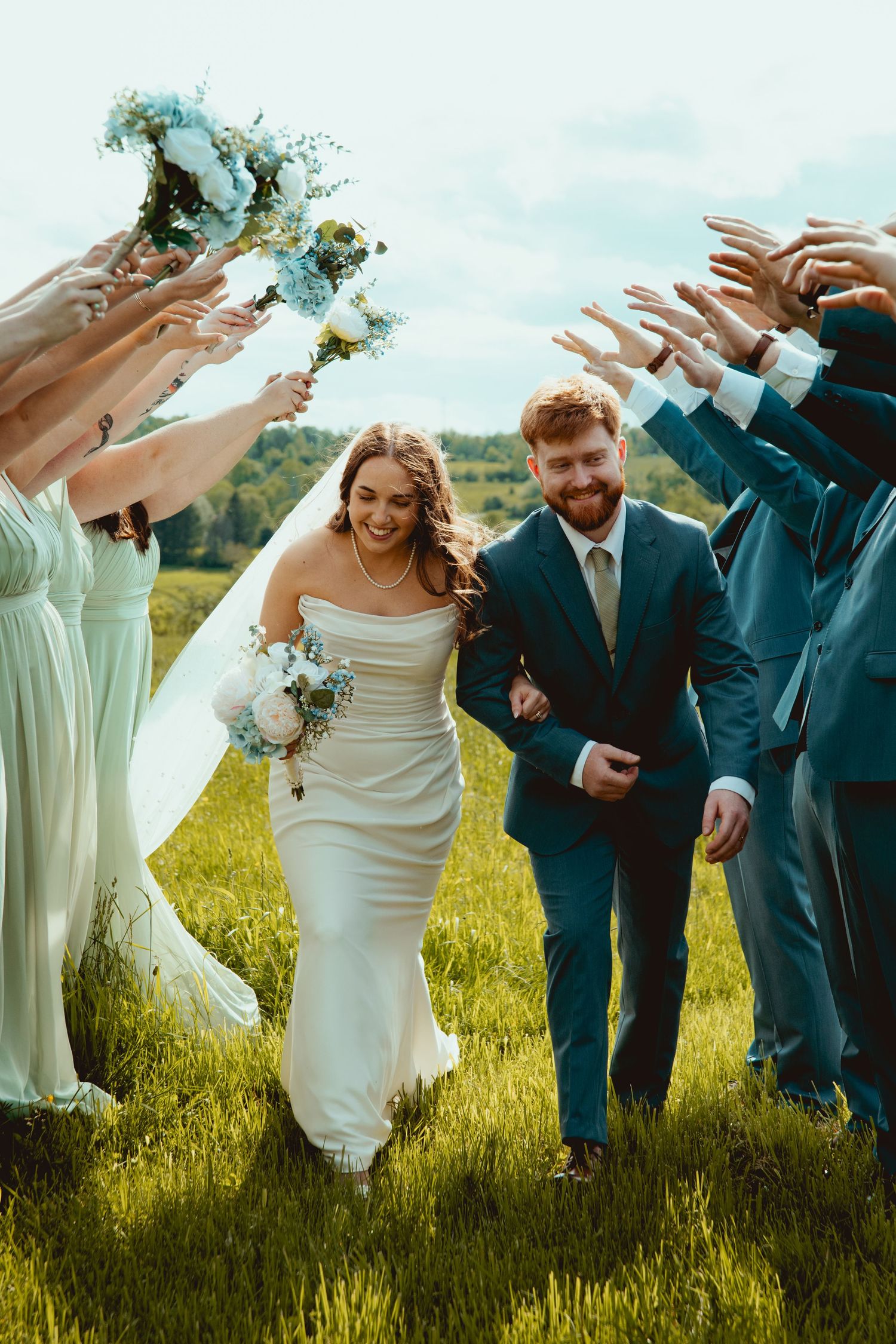 Wedding party celebrates with joyful poses in field with mint bridesmaids dresses.