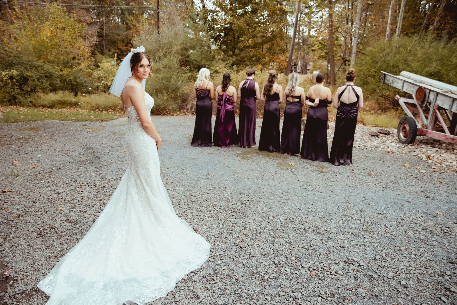 A bride in a white wedding dress twirls and dances on a gravel path outdoors.
