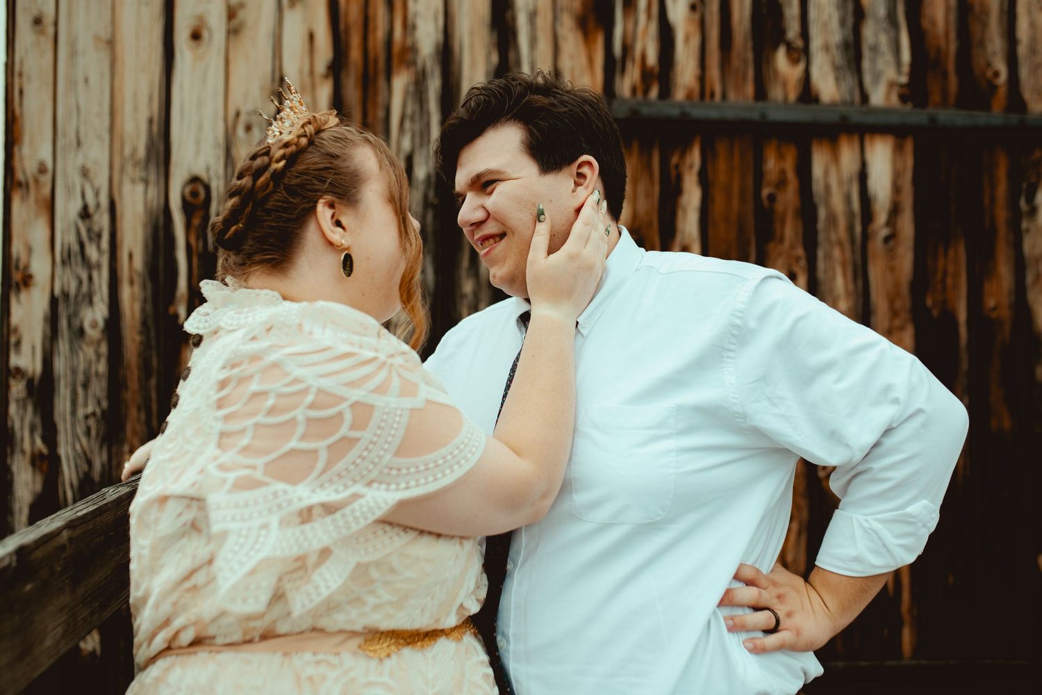 A couple shares an intimate moment against a rustic wooden barn wall.
