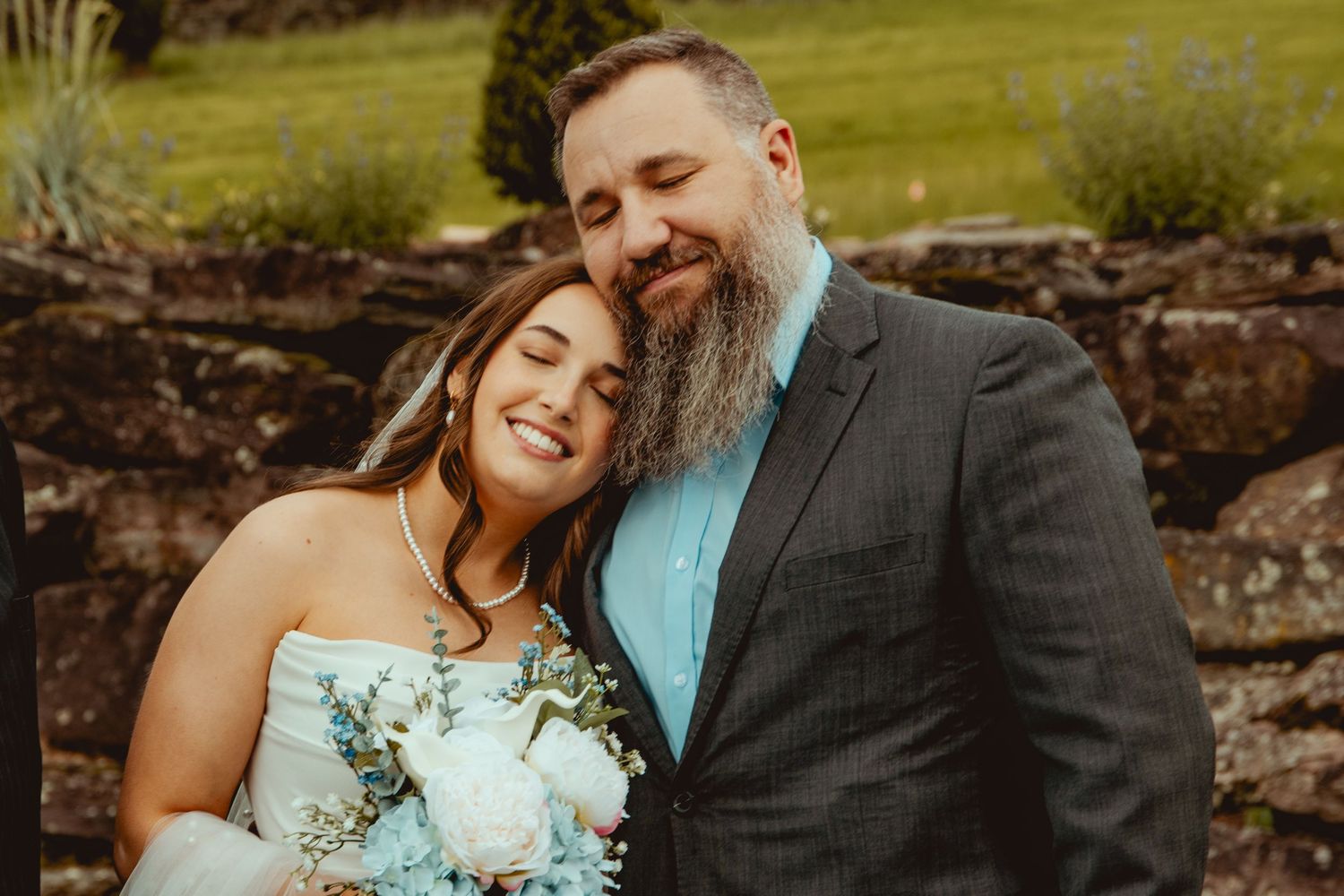 Intimate wedding portraits captured against rustic outdoor scenery with stone wall backdrop.