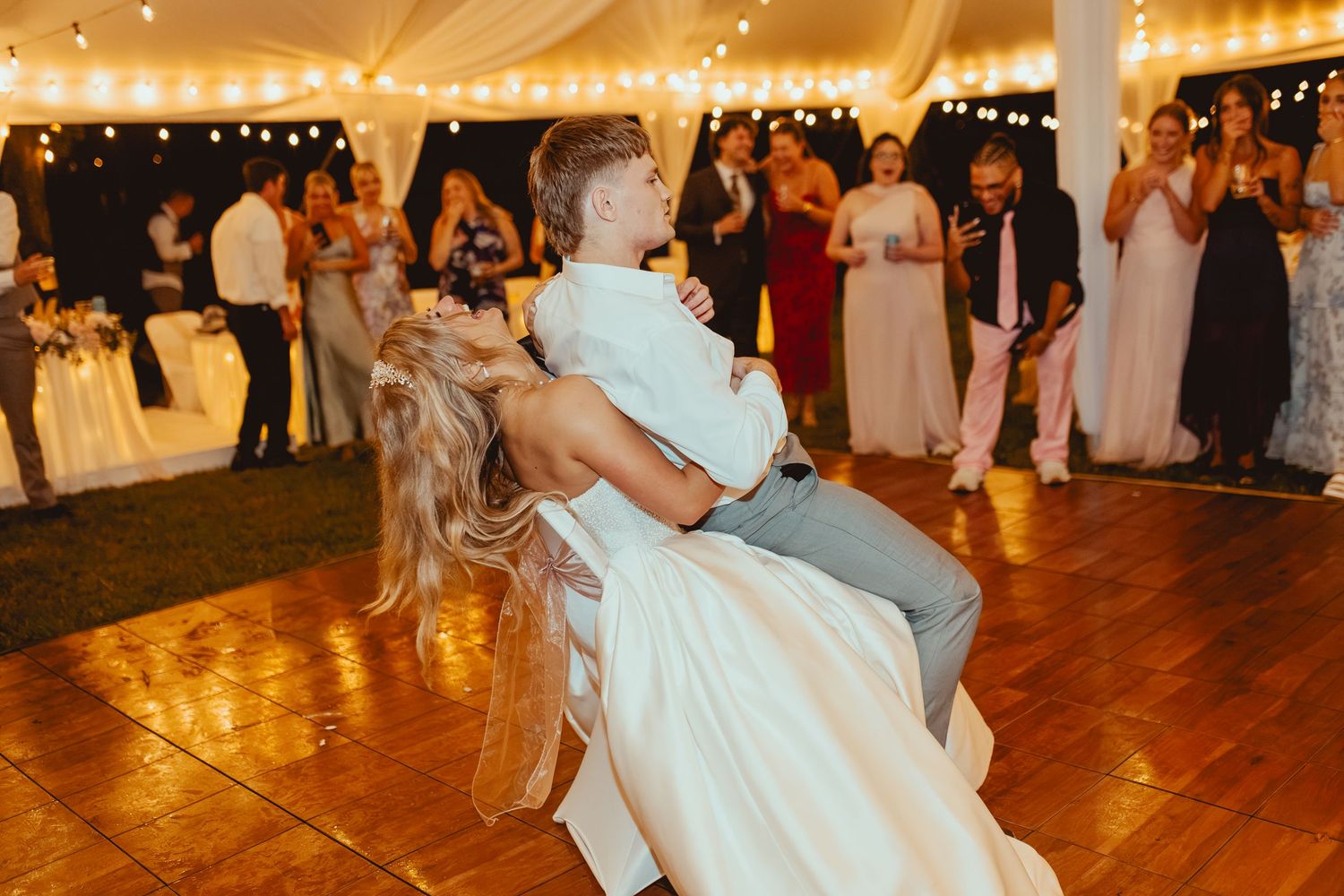 Groom lifts bride during joyful first dance at elegant outdoor wedding reception.